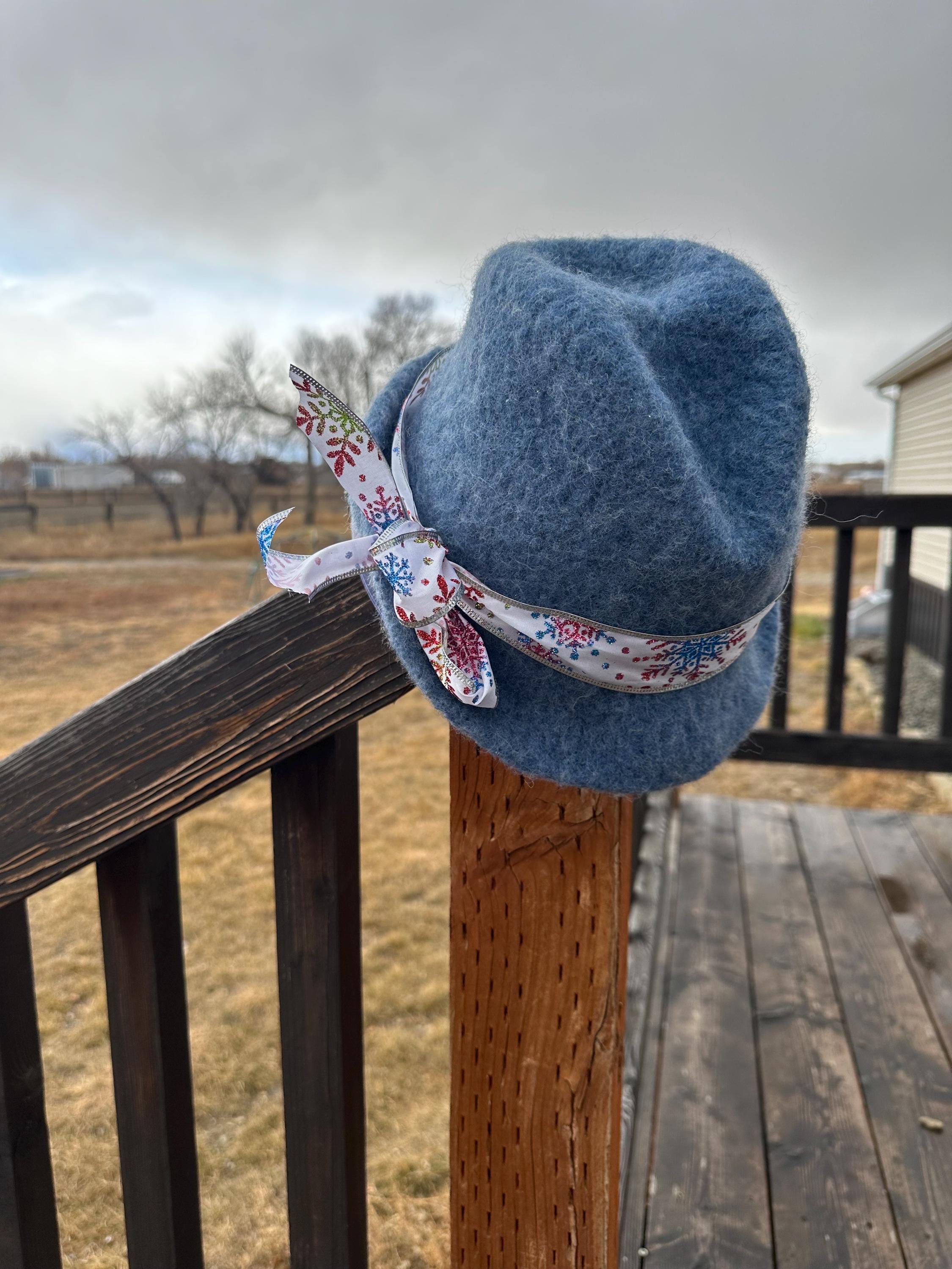 Blue felt hat with a floral ribbon on a wooden railing outdoors.