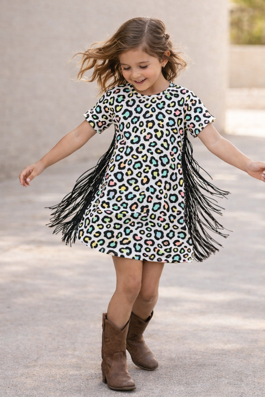 Child wearing a leopard print dress with fringe and brown boots outdoors. GIRLS COLORFUL CHEETAH PRINT DRESS