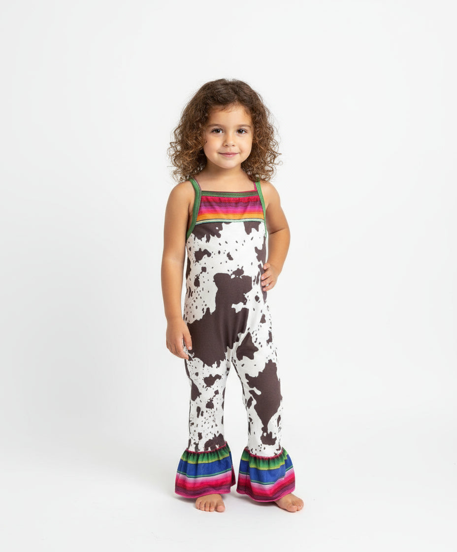 Cowprint Serape Jumpsuit—This stylish Cowprint Outfit features a bold cowprint design complemented by fun pink, blue, and green serape stripes on the neckline, shoulder tie straps, and ruffle hem. Easy 1 piece Cowgirl outfit. Ships FREE with $35+