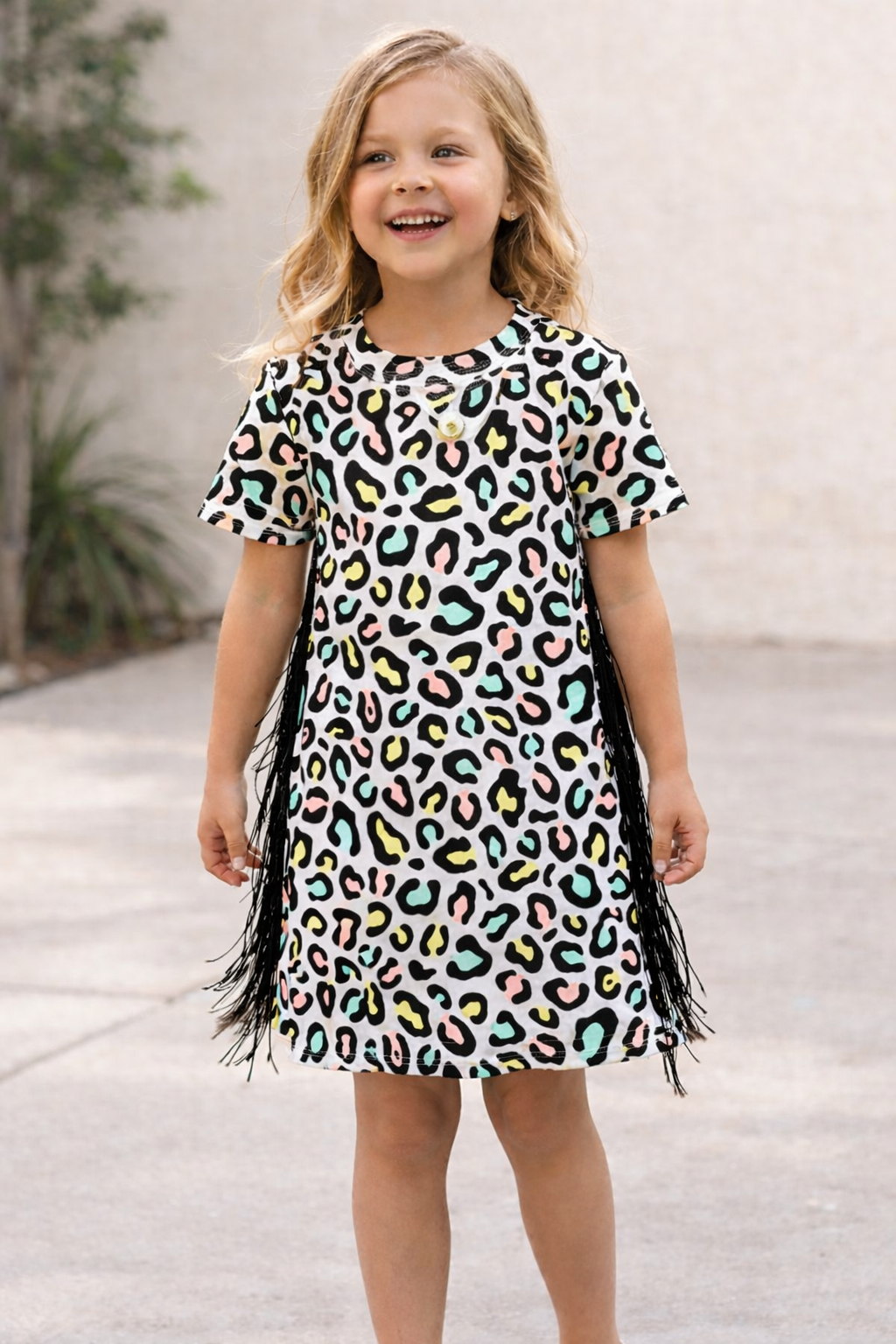Young girl wearing a colorful leopard print dress with fringe details outdoors.