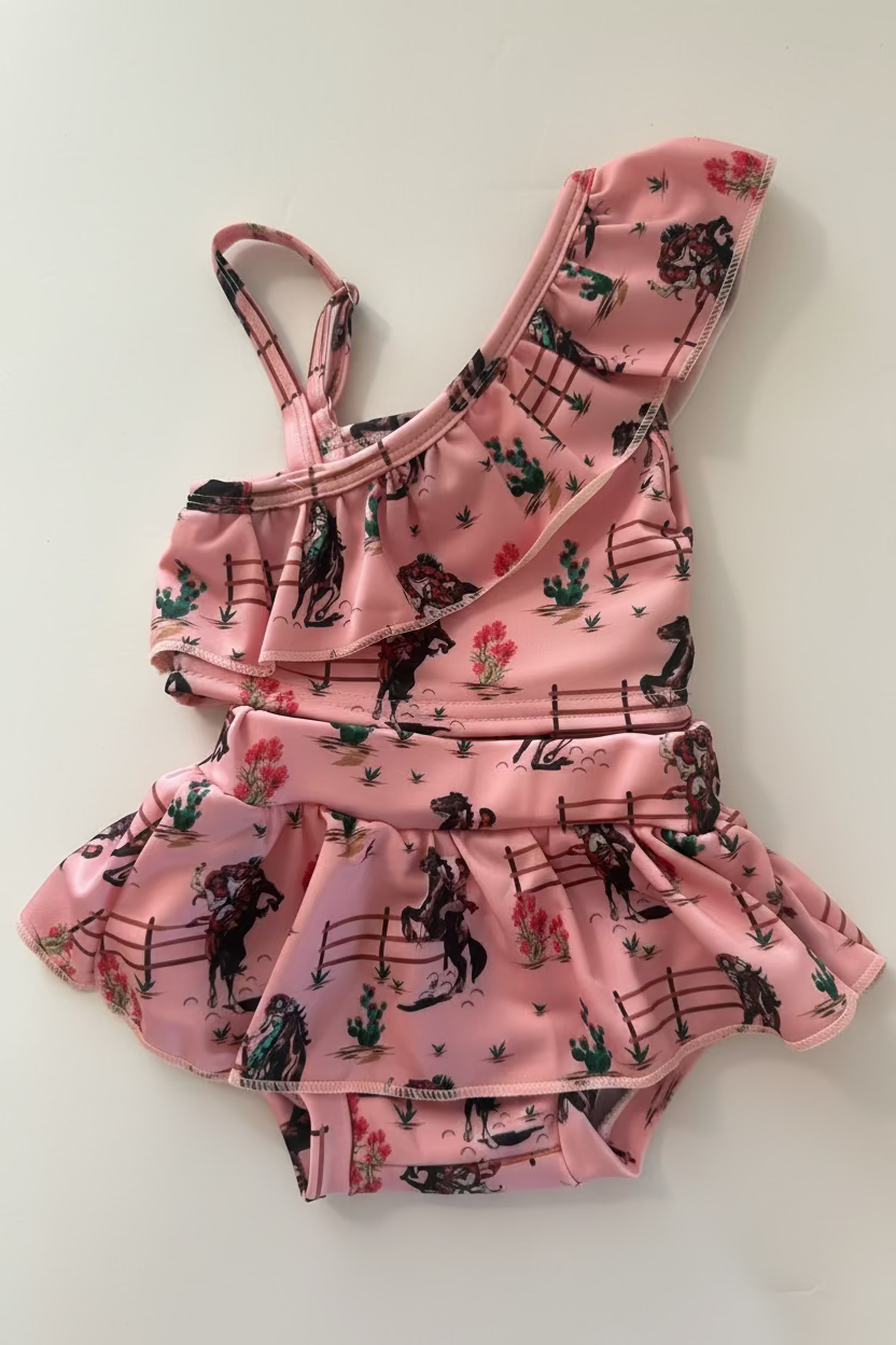 Pink children's swimsuit with cowgirls, horsse and cactus pattern on a white background