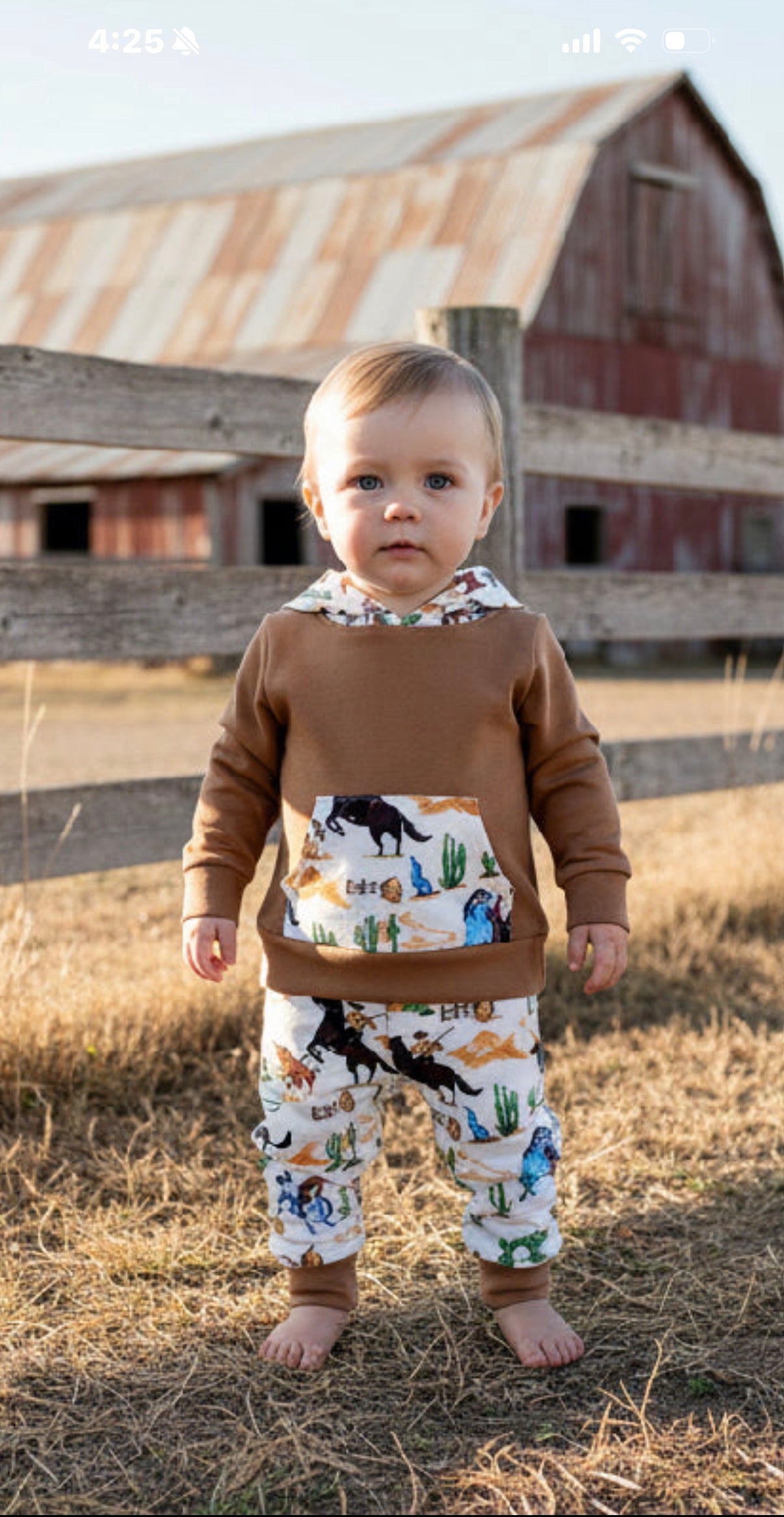 Child wearing a brown cowboy hoodie and retro cowboy pants standing in front of a barn.