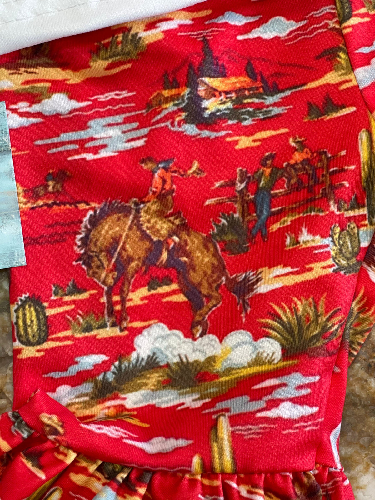 CLOSE UP VIEW OF THE RED BELL BOTTOM PANTS SO YOU CAN SEE THE VINTAGE COWBOY PRINT FABRIC, BUCKING HORSES, CACTI, AND ALL THE SPLENDID COWBOY DETAIL OF THESE WESTERN FLARE PANTS!