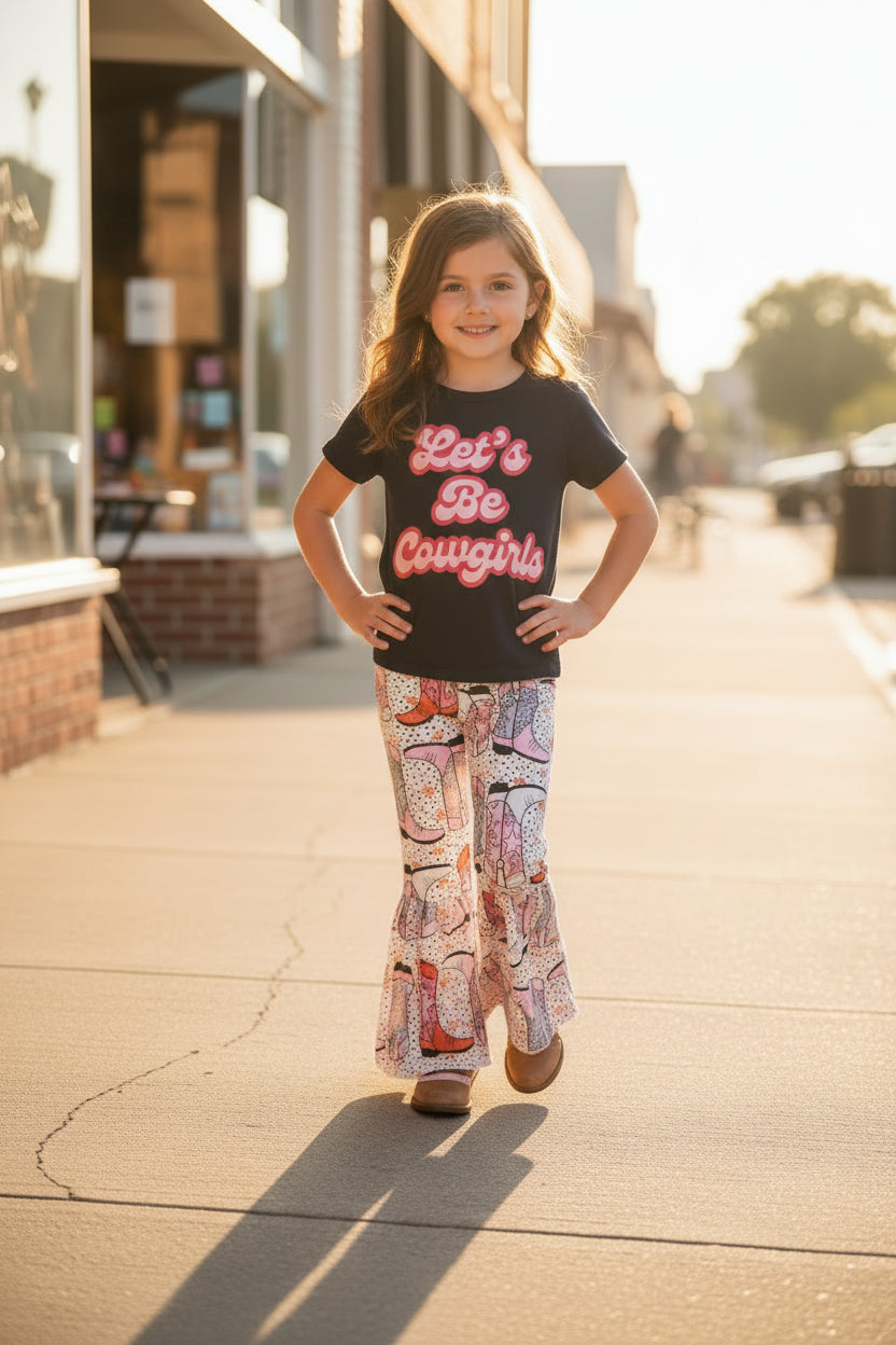 Black t-shirt with 'Let's Be Cowgirls' text and patterned pants with cowboy boot design on a textured surface.