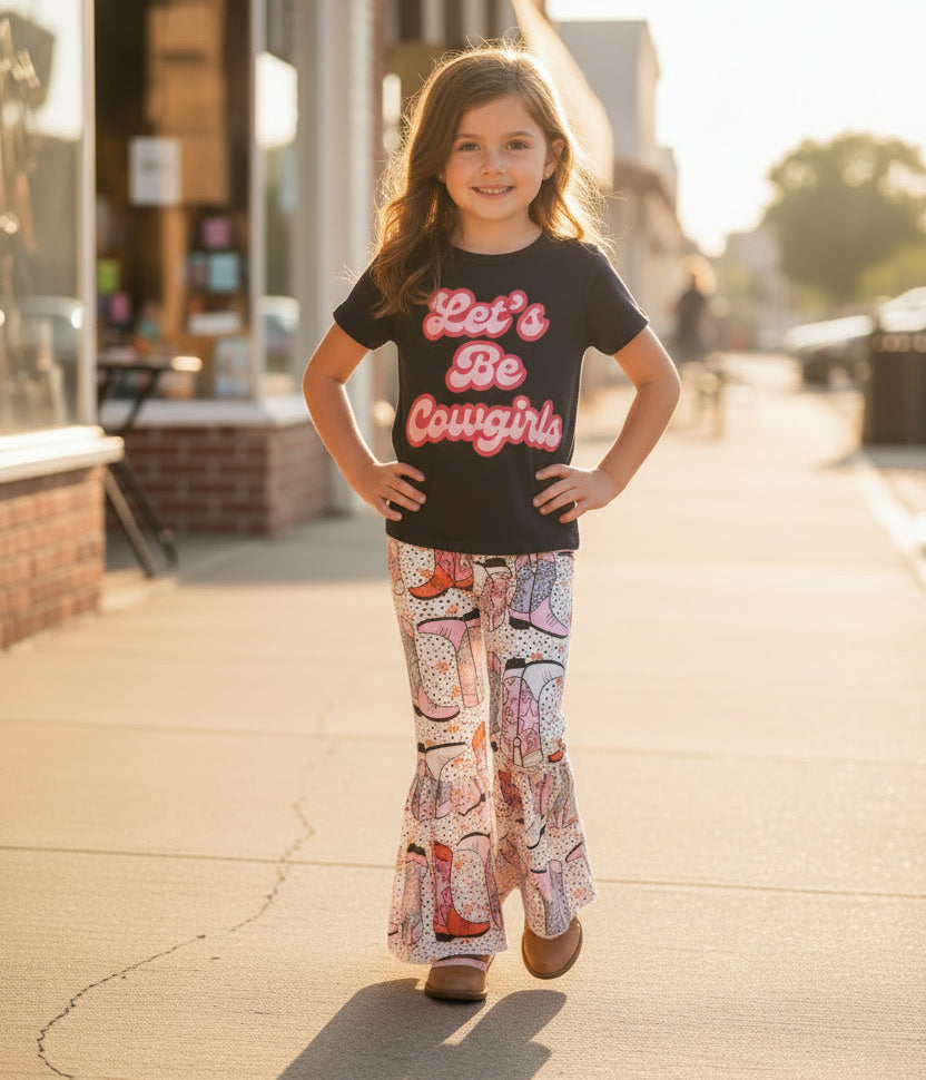 Black t-shirt with 'Let's Be Cowgirls' text and patterned pants with cowboy boot design on a textured surface.
