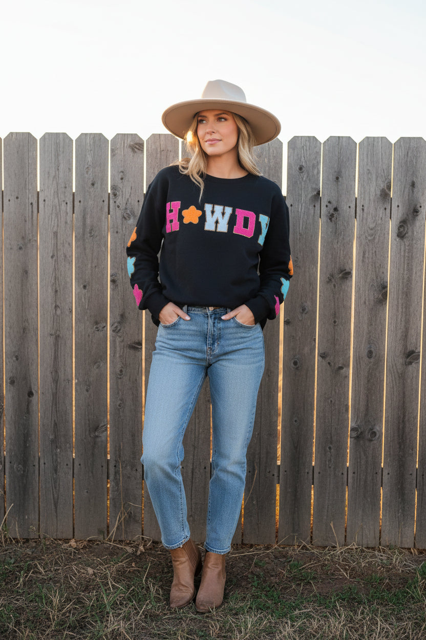 woman standing by fence wearing black western sweatshirt, howdy crewneck with glitter patches