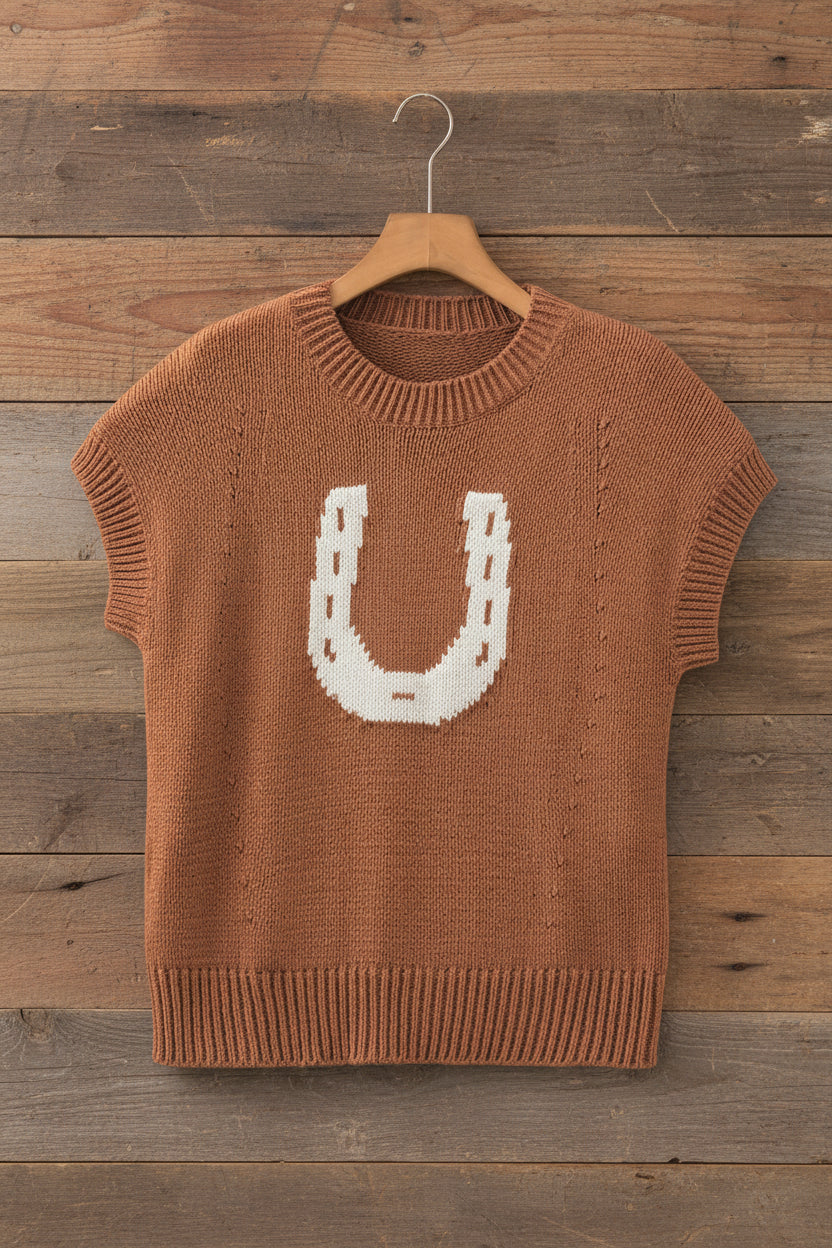 A short-sleeve knit sweater in a warm rust brown color, featuring a large white knitted horseshoe design on the chest, hanging on a wooden hanger against a light gray wall.