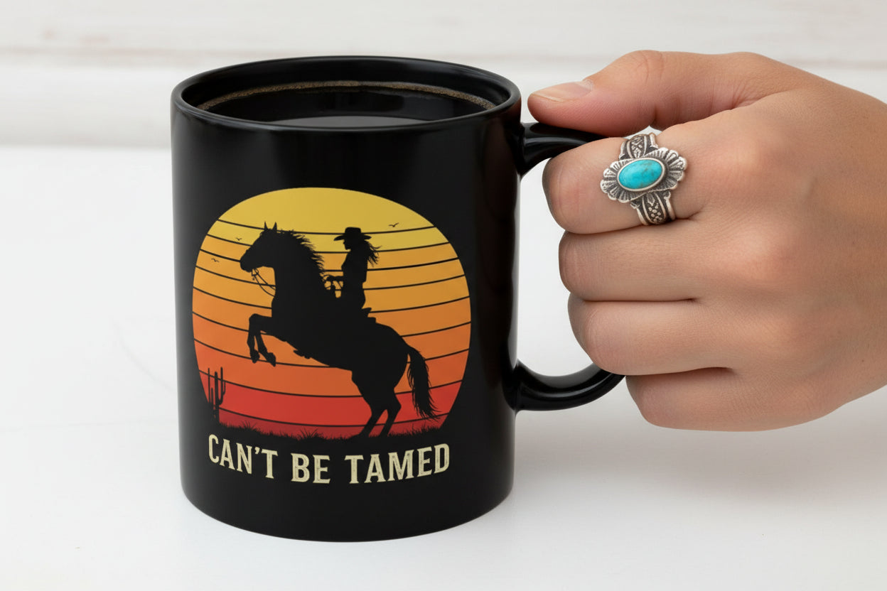 Black mug with a horse and rider design and 'Can't Be Tamed' text held by a womans hand