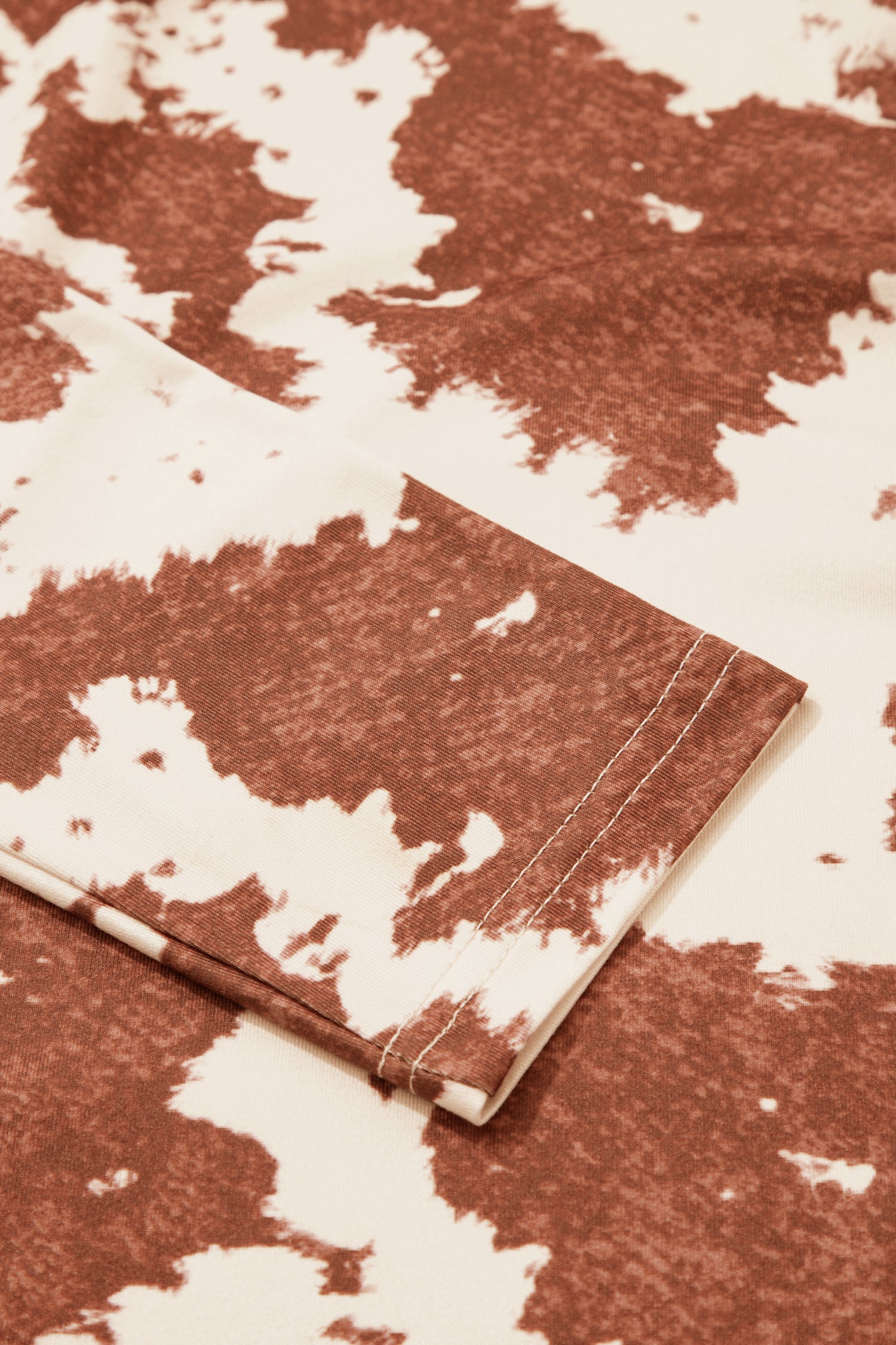 A close-up of brown and off-white cow print pattern, with visible stitching along the hem.