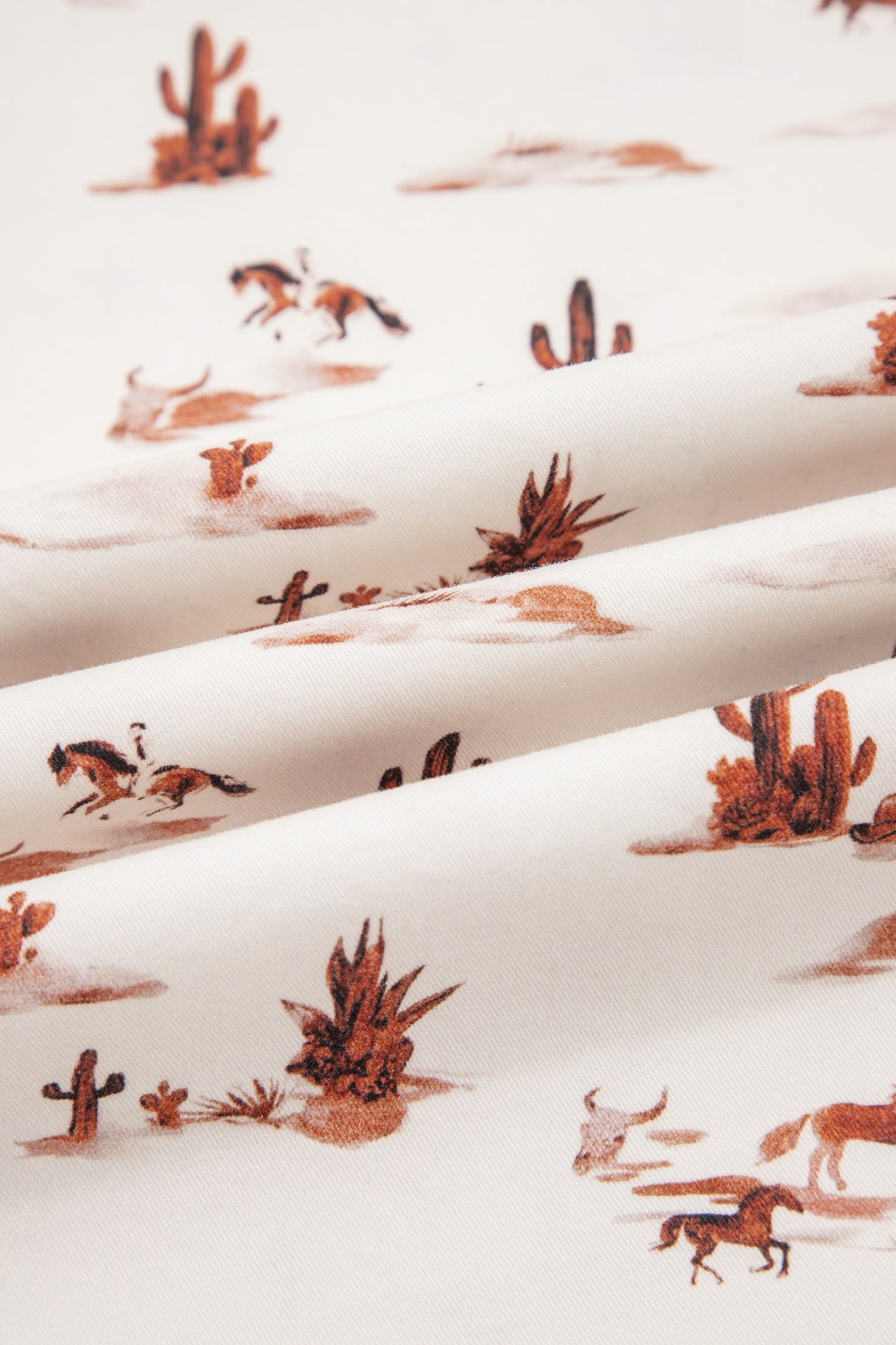 Patterned fabric with desert scene including horses, cacti, and longhorn skulls