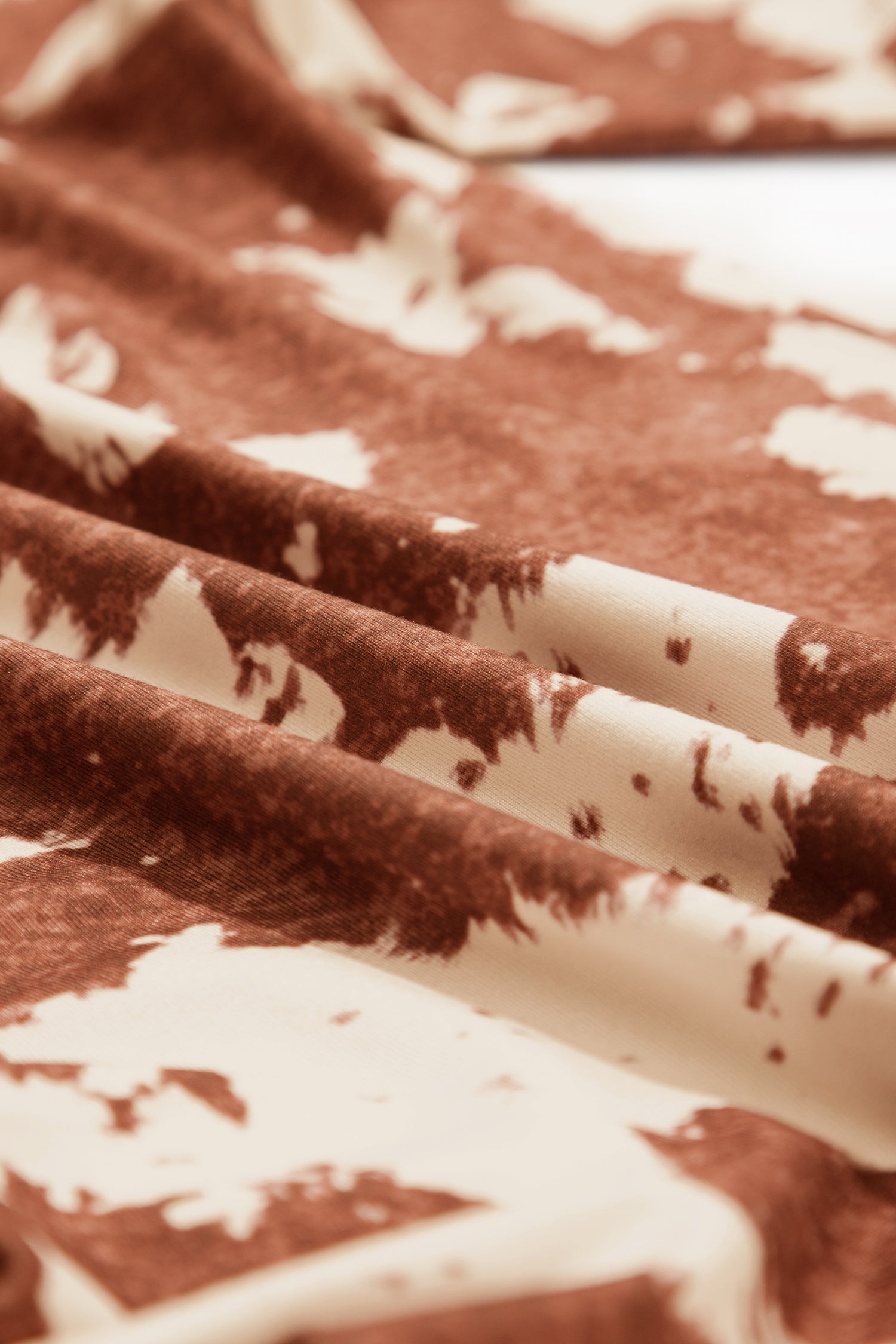 A close-up of draped fabric with a brown and cream cow hide pattern, showing the soft texture and folds.