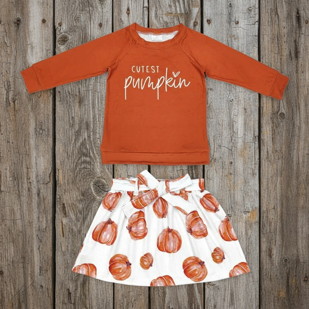 Children's outfit with orange 'Cutest Pumpkin' shirt and pumpkin-patterned skirt on a light gray background