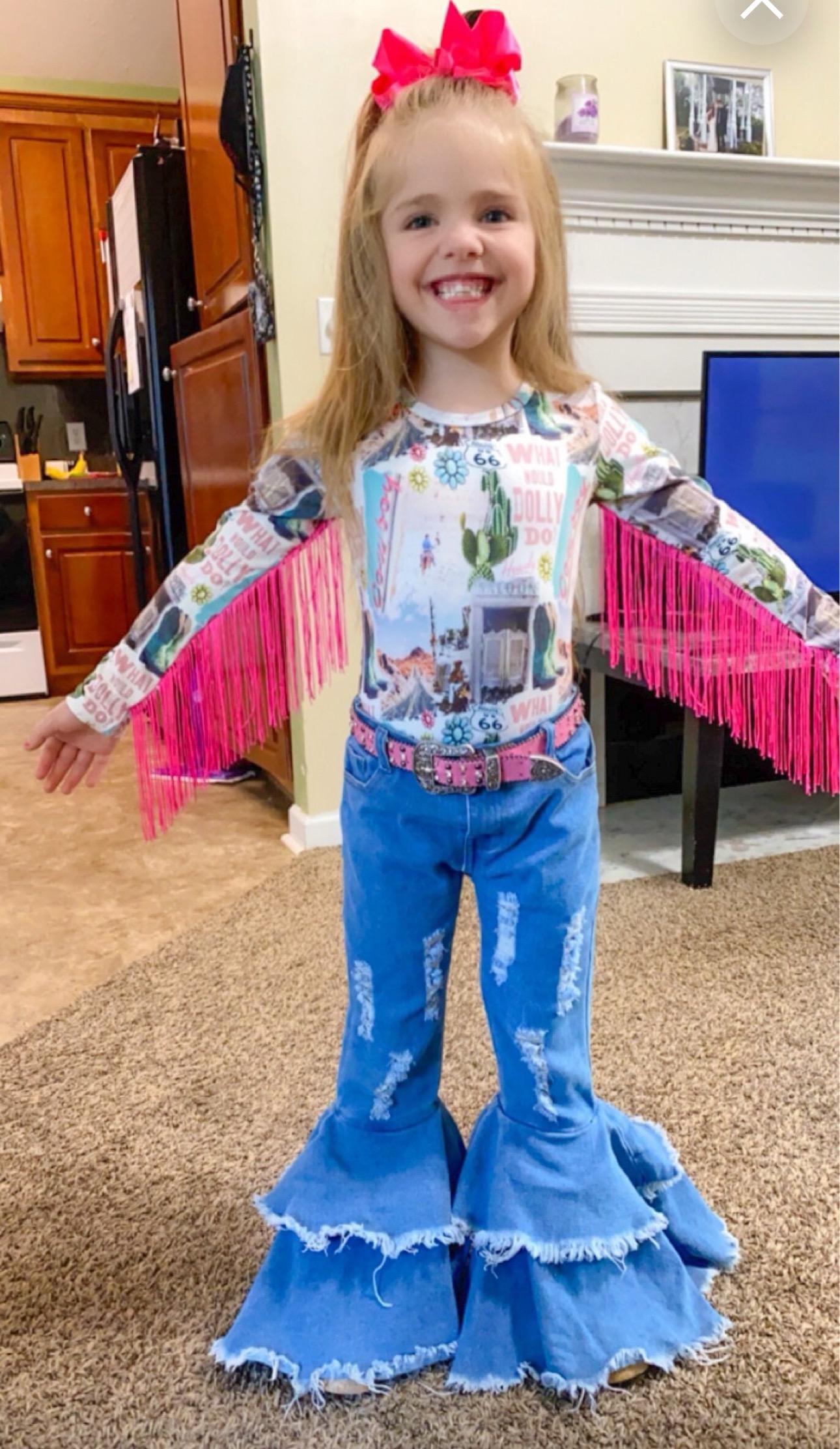 Get ready to dazzle with our adorable What Would Dolly Do? Cowgirl Shirt & Fringe Bodysuit.
The button-up shirt features a bold Western-inspired design, while the fringe bodysuit adds flair in vibrant pink. Shop Razels for Girls Western Wear