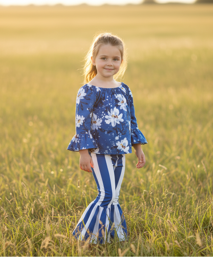 Young girl in a blue floral top and striped pants standing in a field.