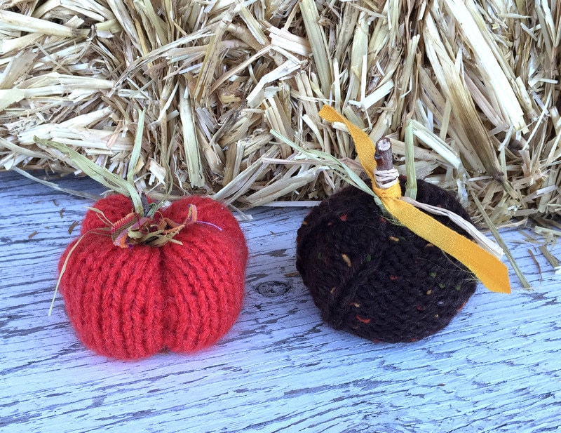 picture of knit pumpkins varying in size from small to large. Pumpkins are hand-knit with a ribbed appearance. The larger pumpkins have knit vines and leaves, while the smaller feature sticks with correlating fabric leaves.