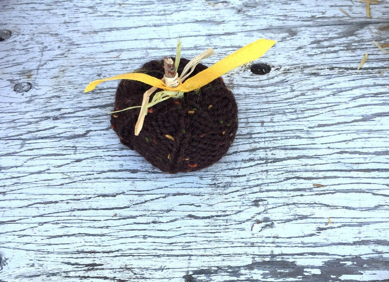 picture of knit pumpkins varying in size from small to large. Pumpkins are hand-knit with a ribbed appearance. The larger pumpkins have knit vines and leaves, while the smaller feature sticks with correlating fabric leaves.