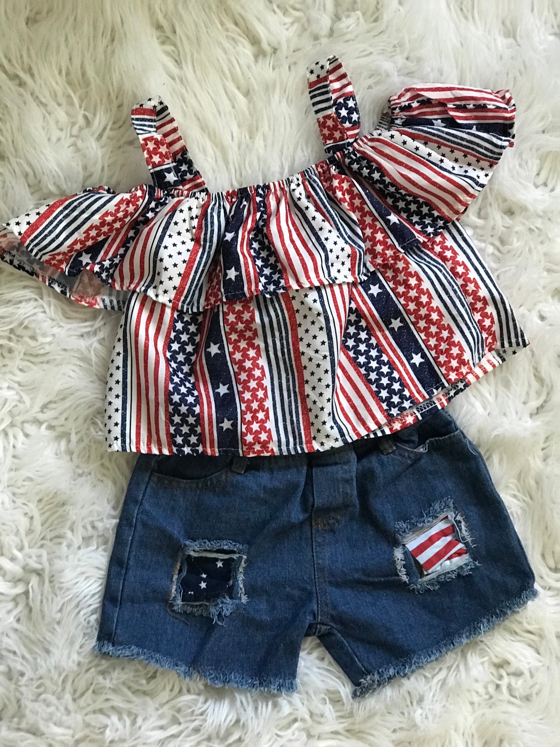 American Girl Short Outfit: The Shorts: The red, white and blue Americana pockets show through the shorts distressing! Shorts have an elastic waist and faux button.
The Shirt: features cold shoulders and an all-around ruffle in USA fabric.