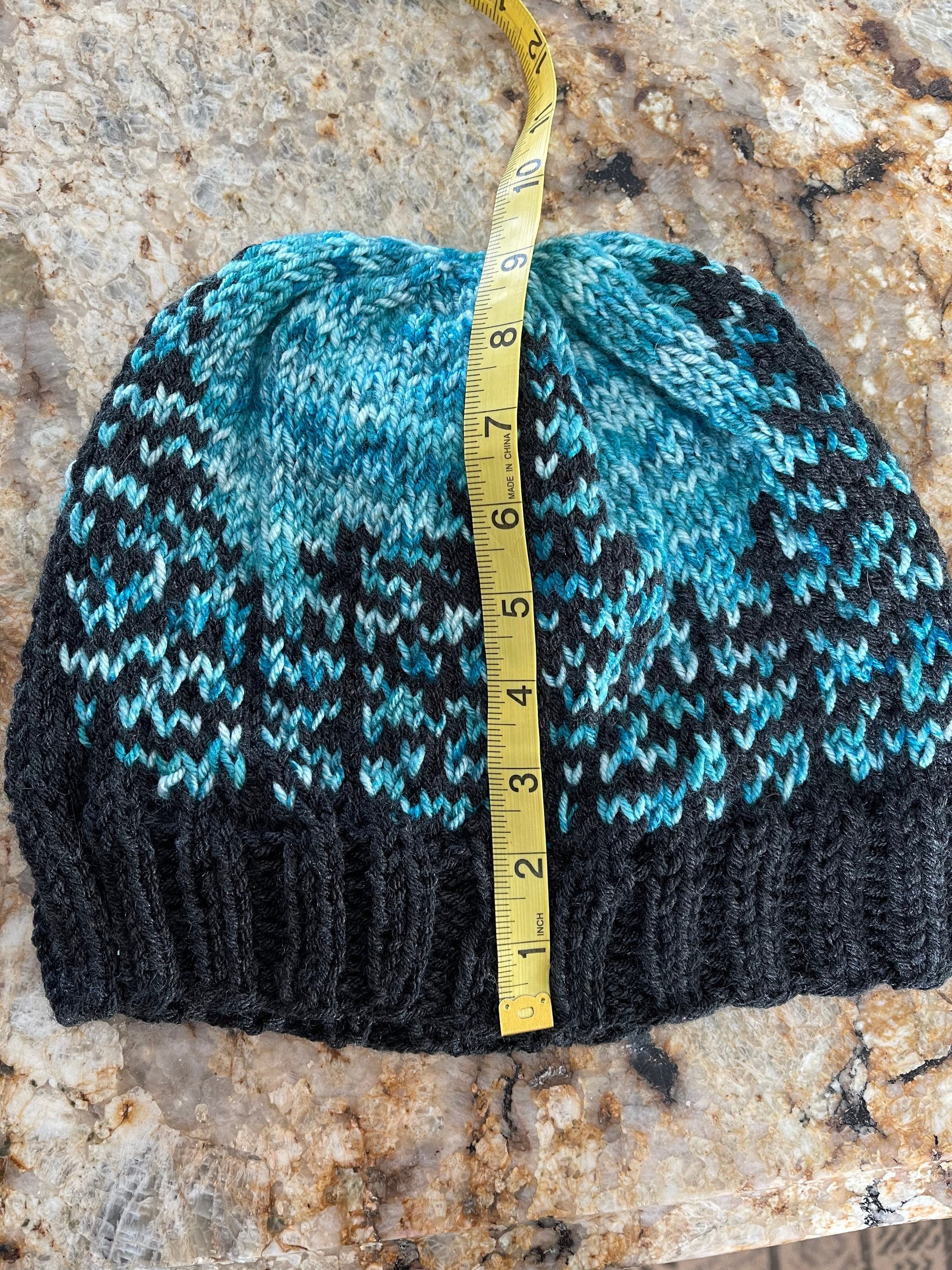 Handknit hat featuring a charcoal grey brim and a forest of trees. The background is beautiful turquoise. This hat is ready to ship and a size large.
