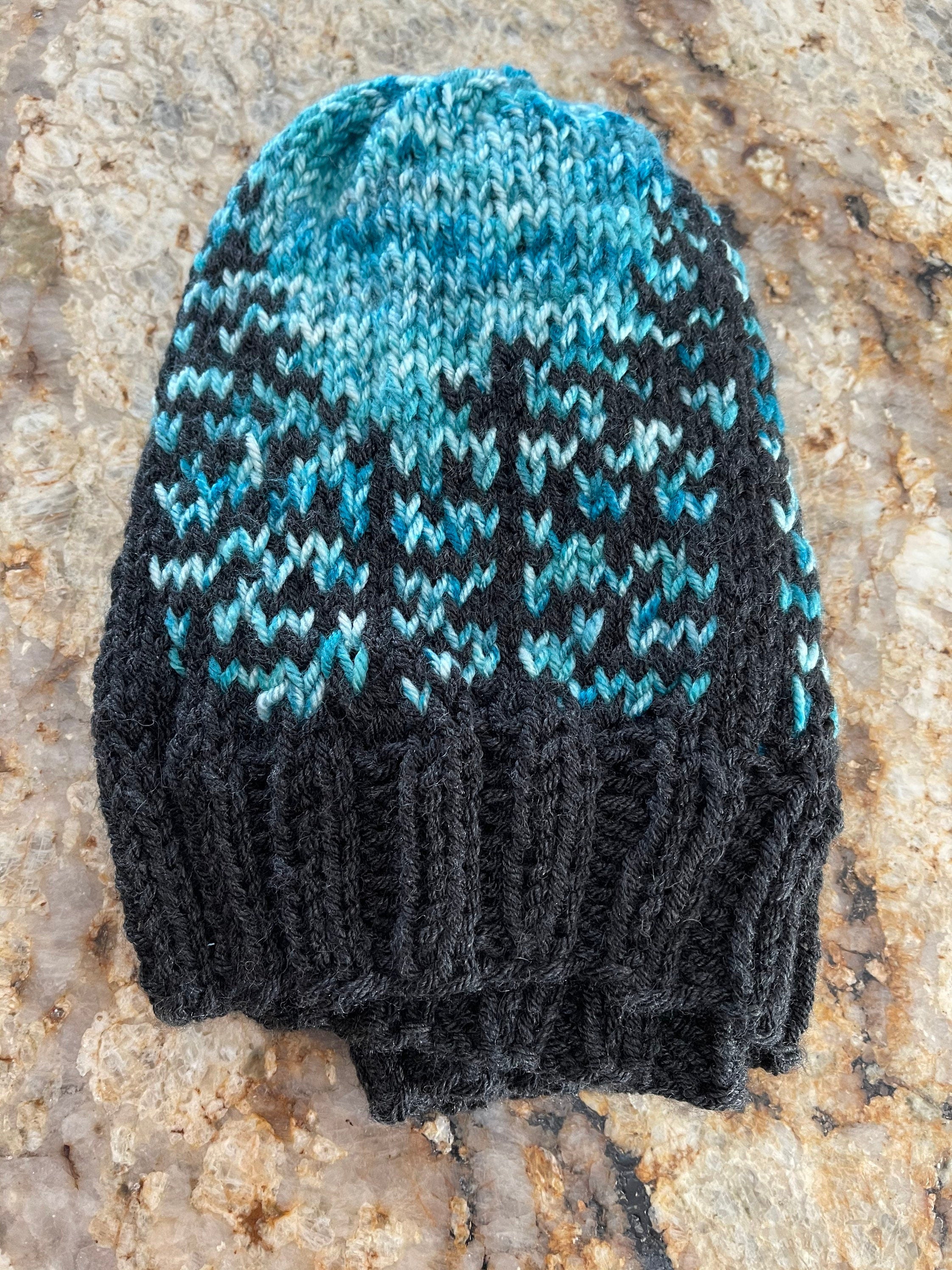 Handknit hat featuring a charcoal grey brim and a forest of trees. The background is beautiful turquoise. This hat is ready to ship and a size large.