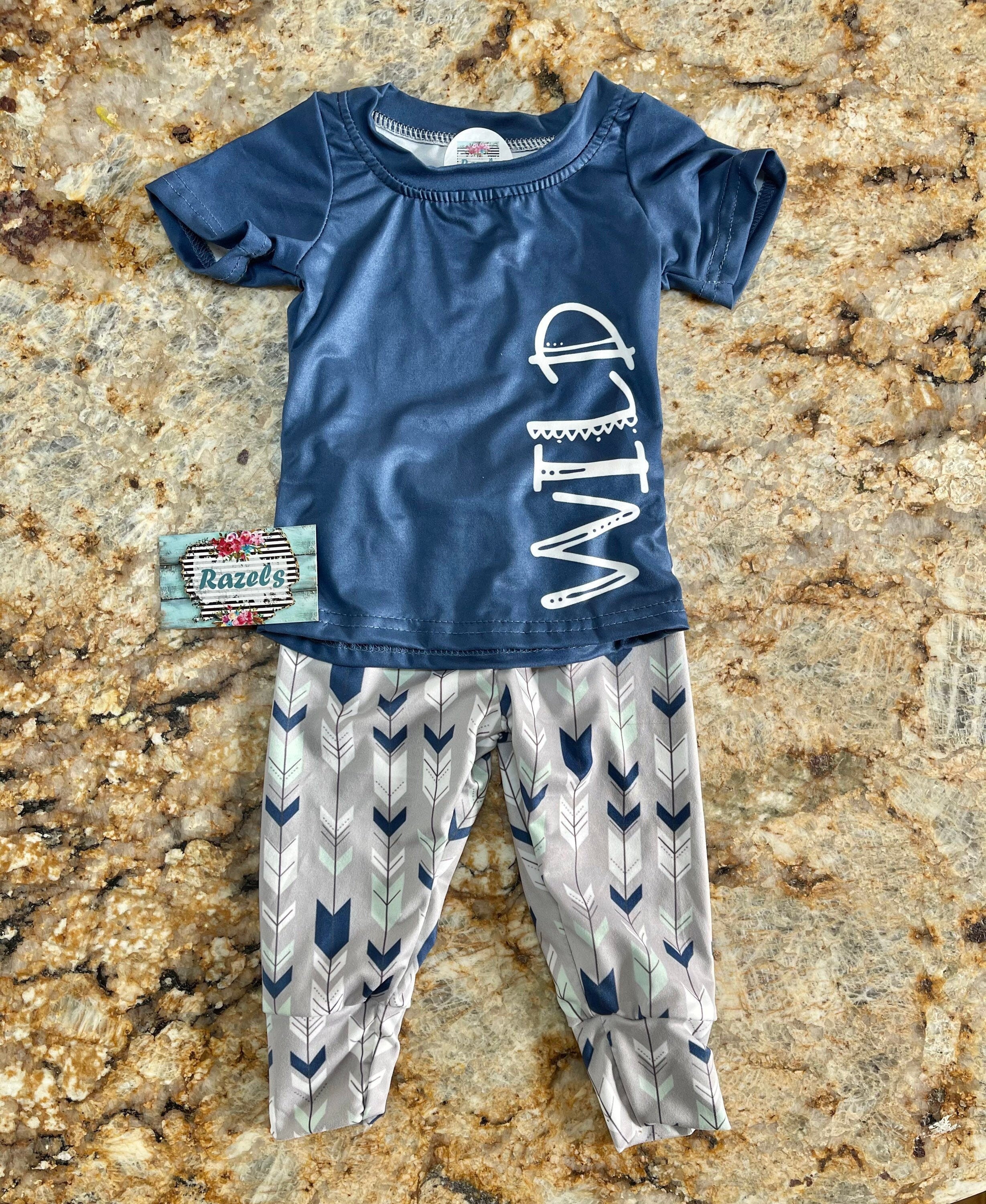 Wild One Jogger Set for Kids! Featuring a bold arrow print on the jogger pants in shades of grey, white, blue, and mint, this set is paired with a striking blue t-shirt that proudly displays "WILD" down the front. Ships FREE with $35+ purchase