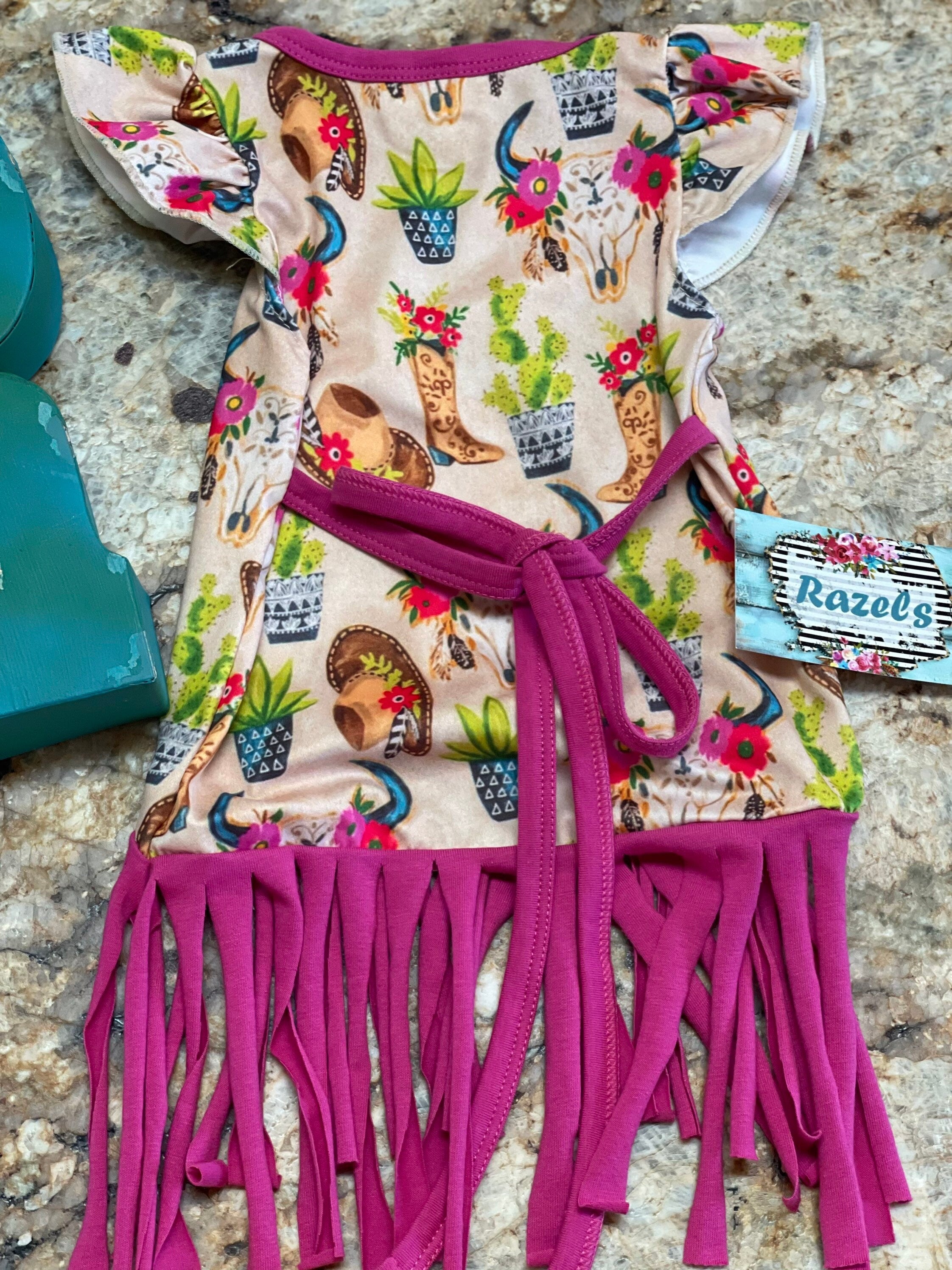 Cowgirl Fringe Dress โ The Perfect Western Tunic for Little Cowgirls features a vibrant western print, flutter sleeves, a charming tie-back, and thick pink fringe. Let your little cowgirl shine in this Cowgirl Fringe Tunic Dress!