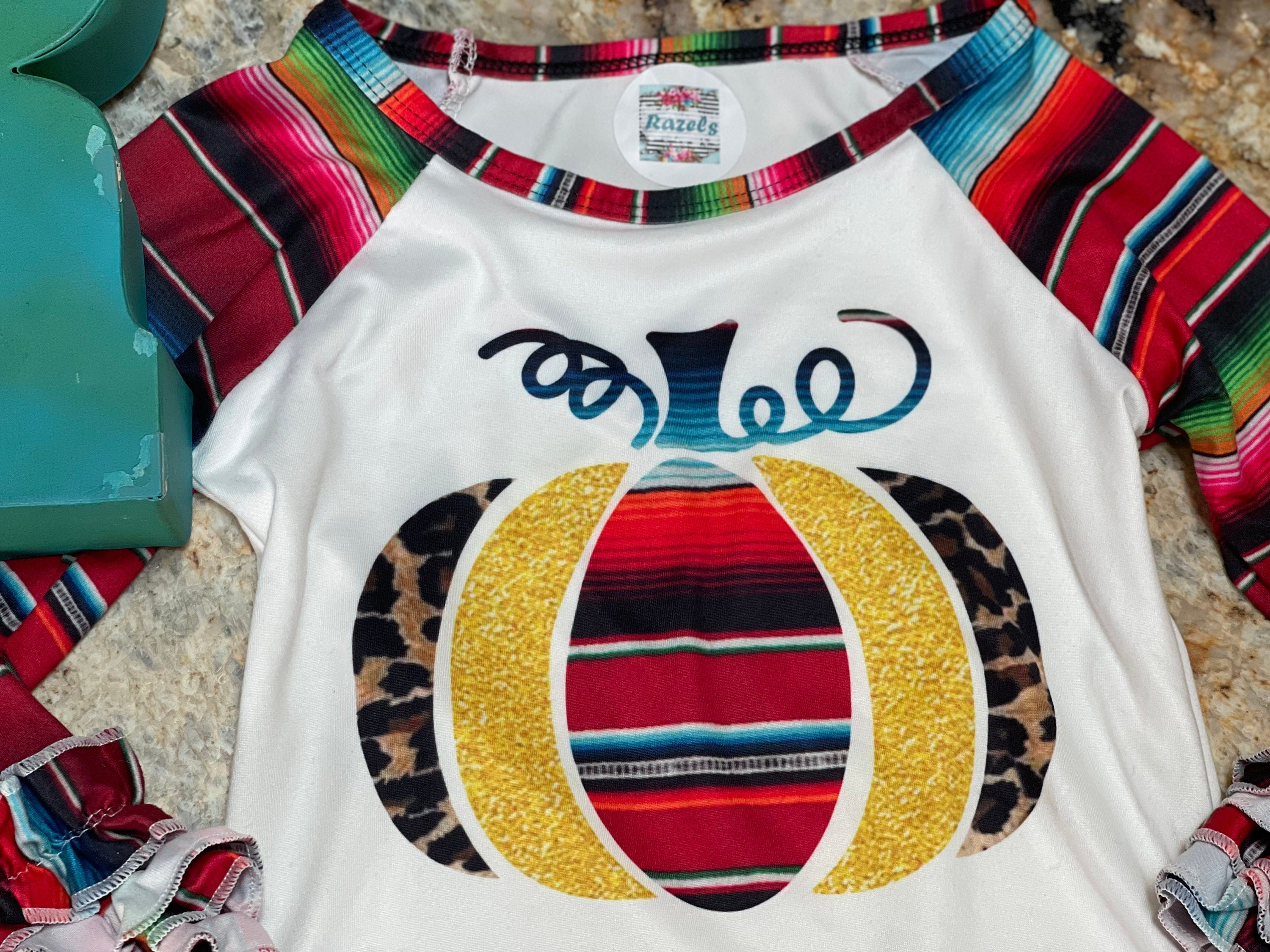 Fall Stripes Pumpkin Ruffle Sleeve Shirt. This Fall Shirt features a pumpkin with Fall serape stripes, cheetah print and glitter gold. The neckline and sleeves are festive serape stripes with wrist ruffles. So cute!