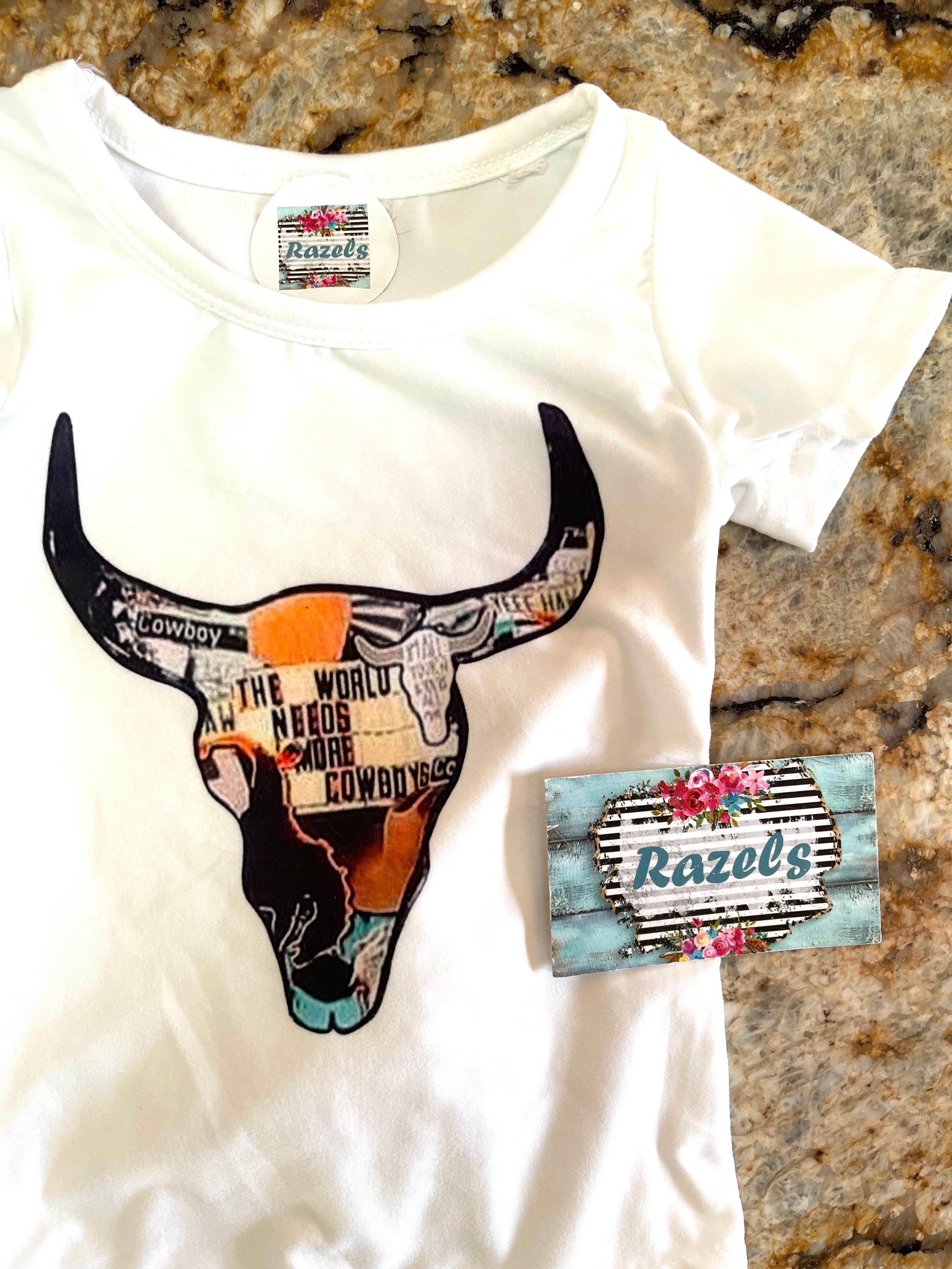 White tshirt with a cowskull that has a cowboy mosaic pattern and the words "The WorldNeeds More Cowboys"