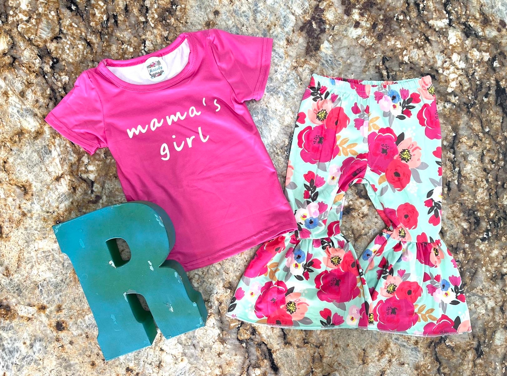 Mama's Girl Bell Bottom Outfit featuring a hot pink t-shirt with Mama's Girl proudly scrolled across the front. The flower bell bottoms are so fun and bright with shades of pink against a mint green background.