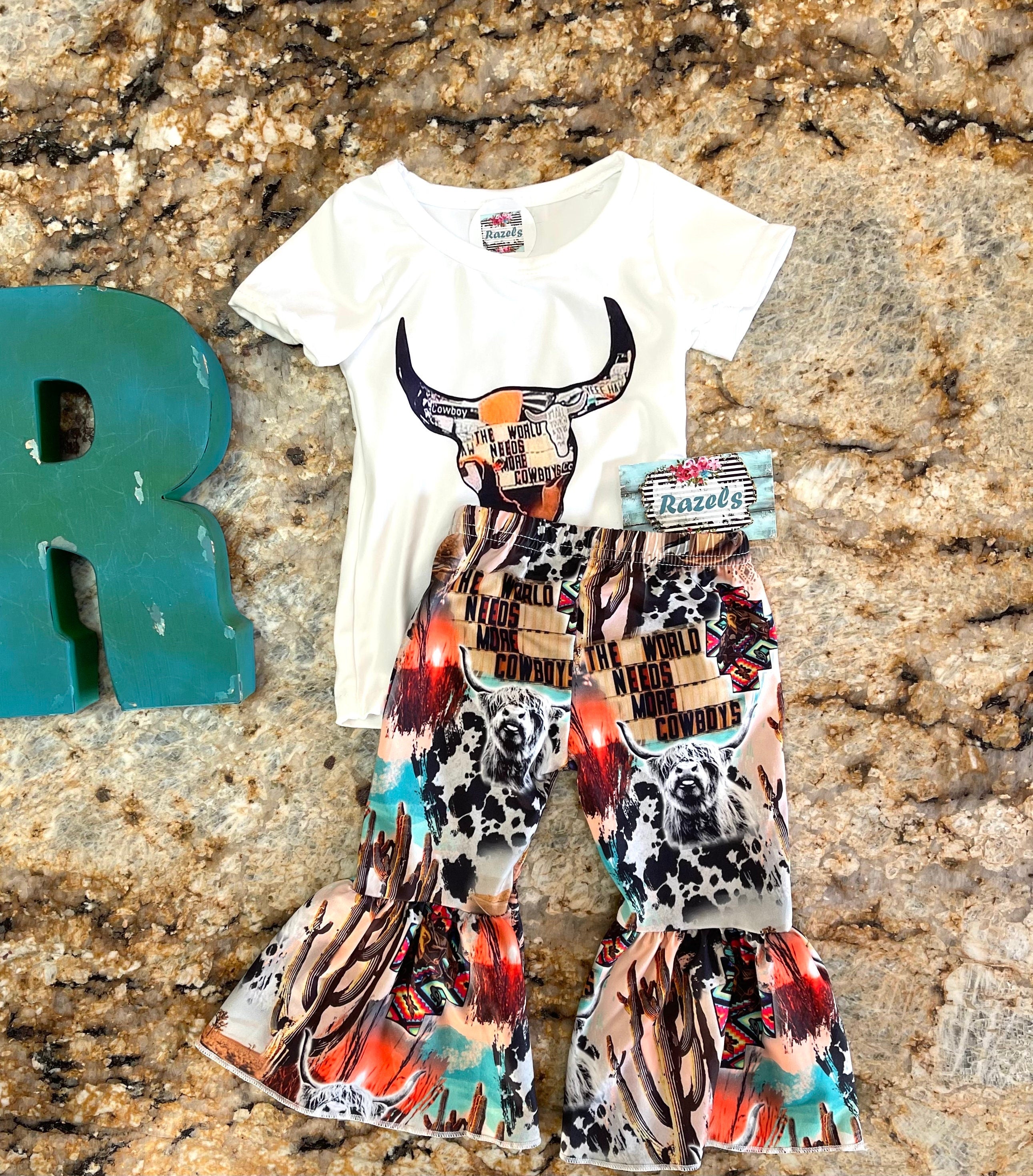 The WorldNeedsMore Cowboys Bell Bottom Outfit, bell bottom pants are a mosaic of Scottish highlander cows, cowprints and cactus. Tshirt features a mosaic inside a cow skull stating the world needs more Cowboys
