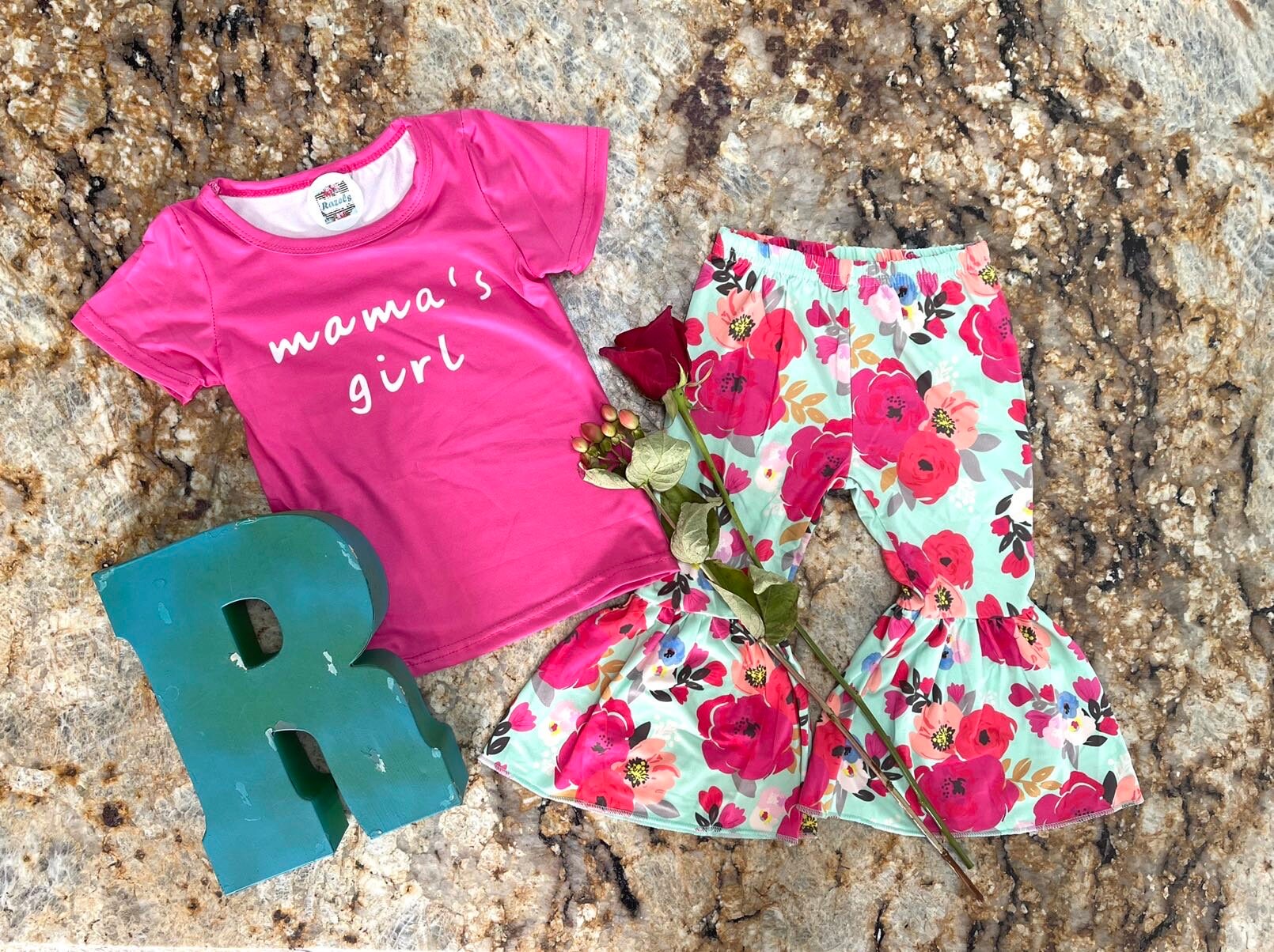 Mama's Girl Bell Bottom Outfit featuring a hot pink t-shirt with Mama's Girl proudly scrolled across the front. The flower bell bottoms are so fun and bright with shades of pink against a mint green background.