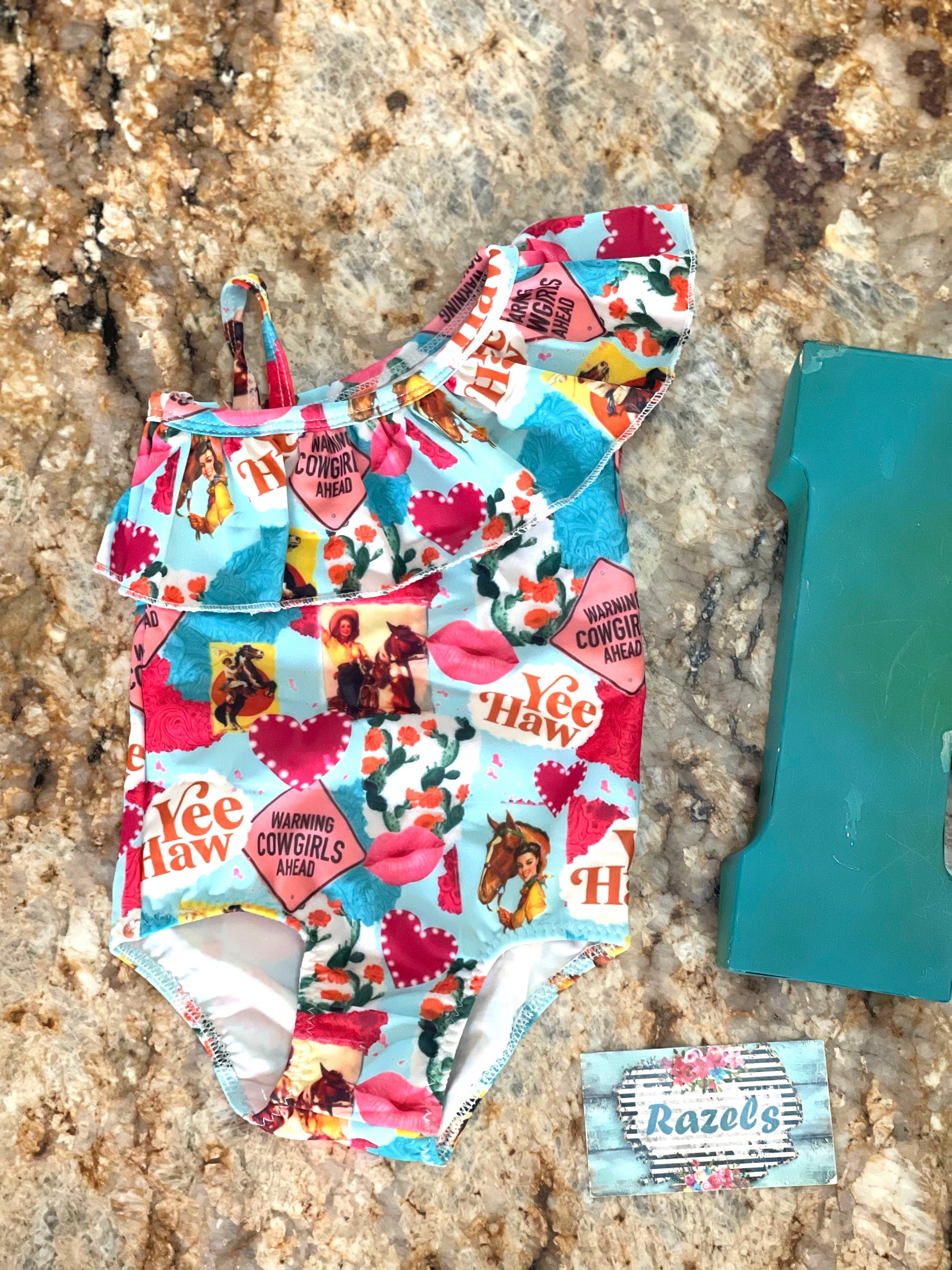 What a fun Cowgirl swimsuit!! 💗 Yeehaw!! Talk about Western Cutie! This fabulous 1-piece girls swimsuit features all the things we love about our Cowgirls - riding horses, hearts, cactus...a warning! So cute! I love this fabric so much it's also available in a girls blouse! 💞 • Available in sizes 0-3 months - 8/9!  • Double layered front More Razels! Check out all our Western swimsuits and sibling swimwear. Ships FREE with $35+ purchase.
