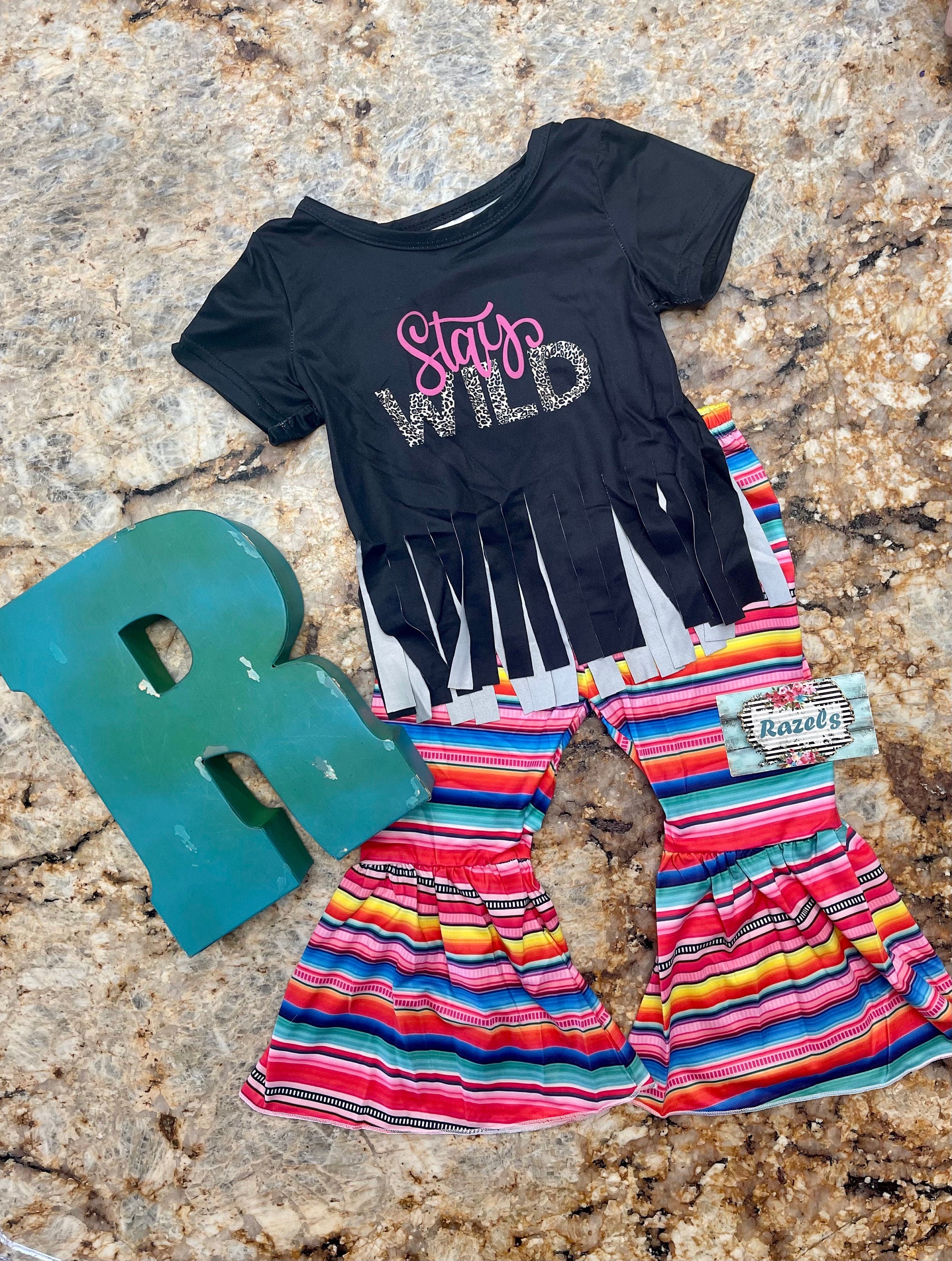 Stay Wild Girls Bell Bottom Set. Features a black Fringed Shirt with a bold "Stay Wild" design in pink and cheetah print, perfectly paired with vibrant serape-striped bell bottoms. Ships FREE with $35+ purchase.