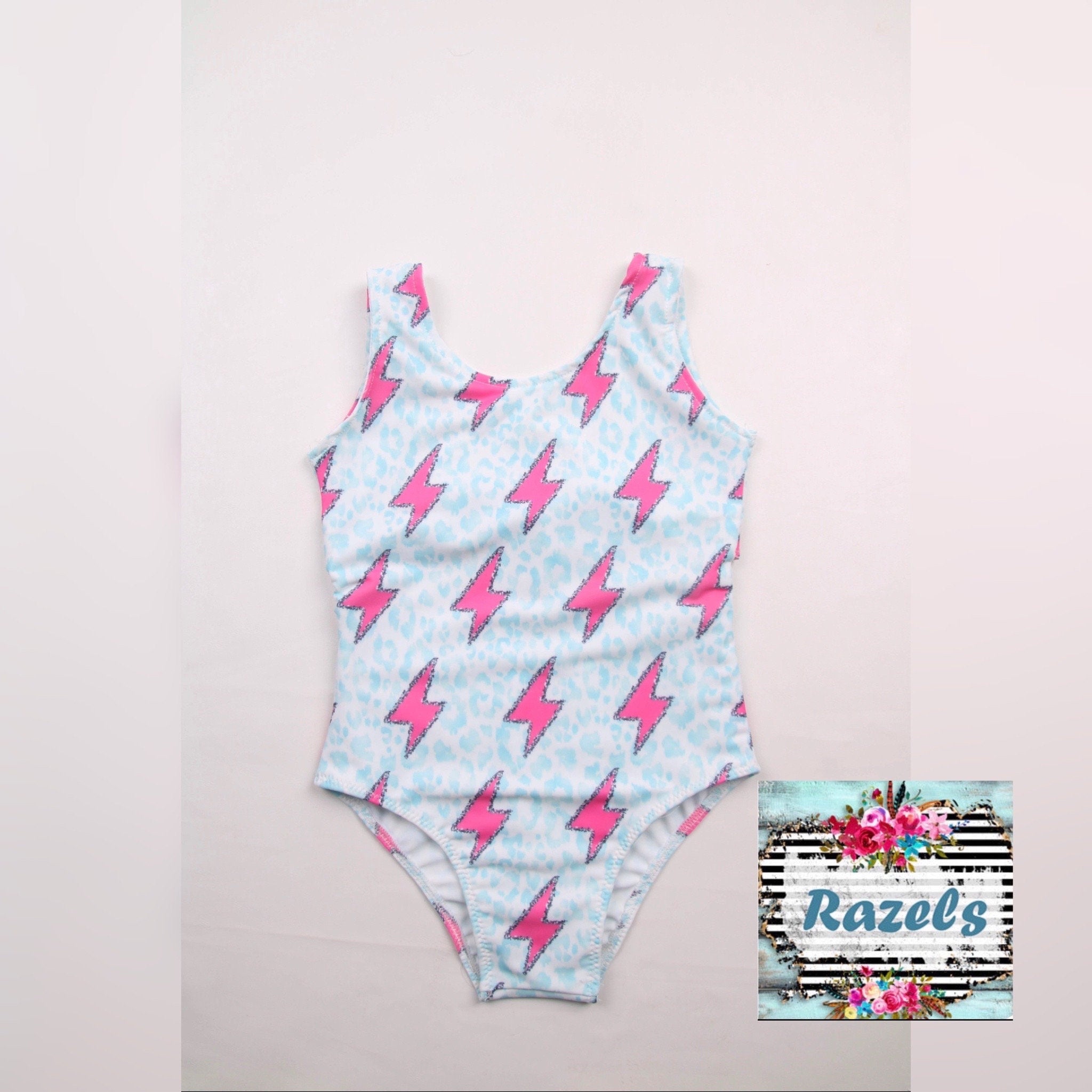 Pink Lightning Bolt One- piece Swimsuit is a Turquoise Cheetah Print One-Piece swimsuit featuring a striking pink lightning bolts and turquoise cheetah print design with a tie-back detail. Available in sizes 0/3 months to 8/9 years. Ships FREE $35+