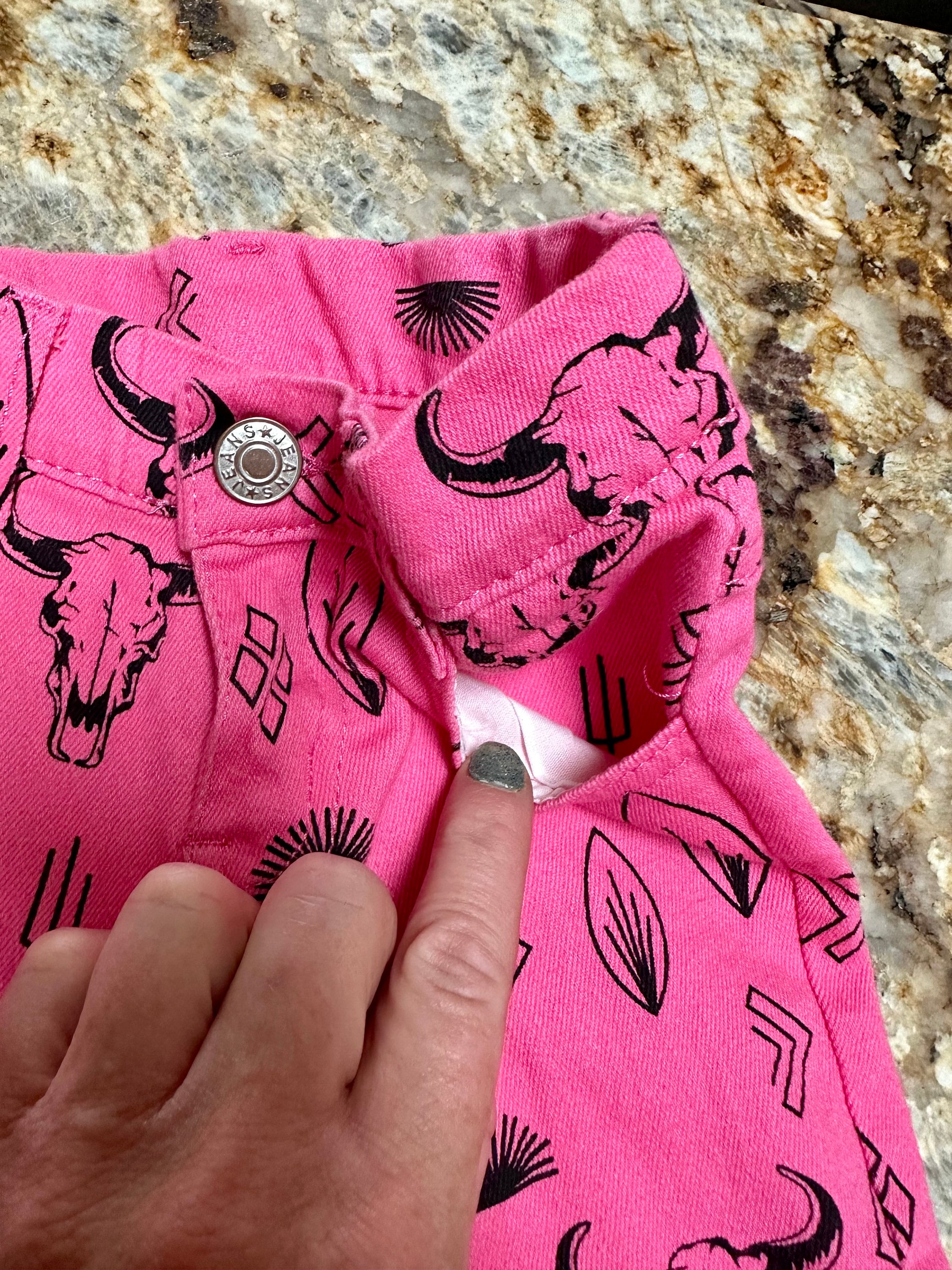 Girls Western Hot Pink Jeans. Jeans feature black steerheads, arrows, and cacti in an awesome western motif. Jeans have an adjustable waistband, pockets, and a frayed bell bottom hem.