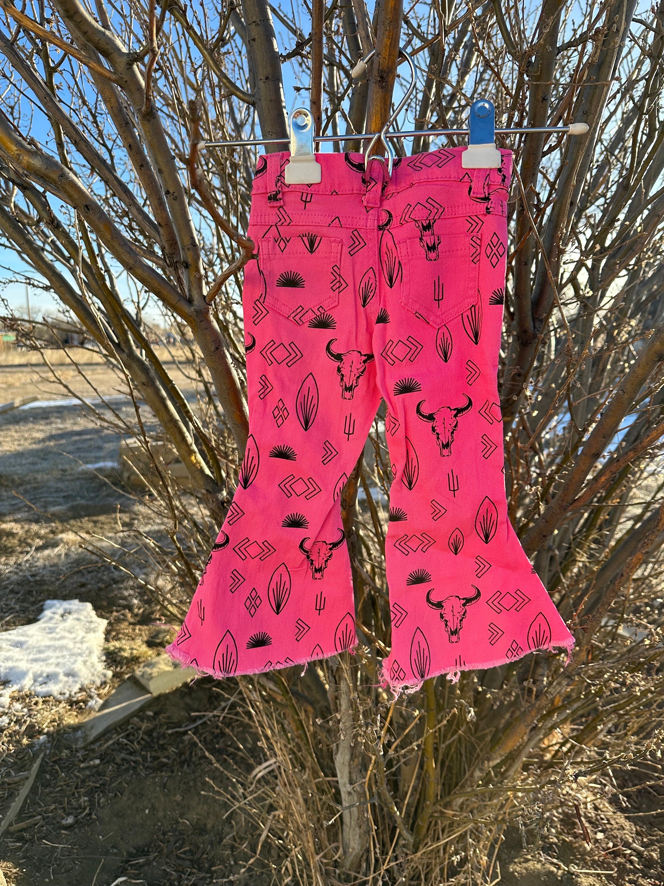 Girls Western Hot Pink Jeans. Jeans feature black steerheads, arrows, and cacti in an awesome western motif. Jeans have an adjustable waistband, pockets, and a frayed bell bottom hem.