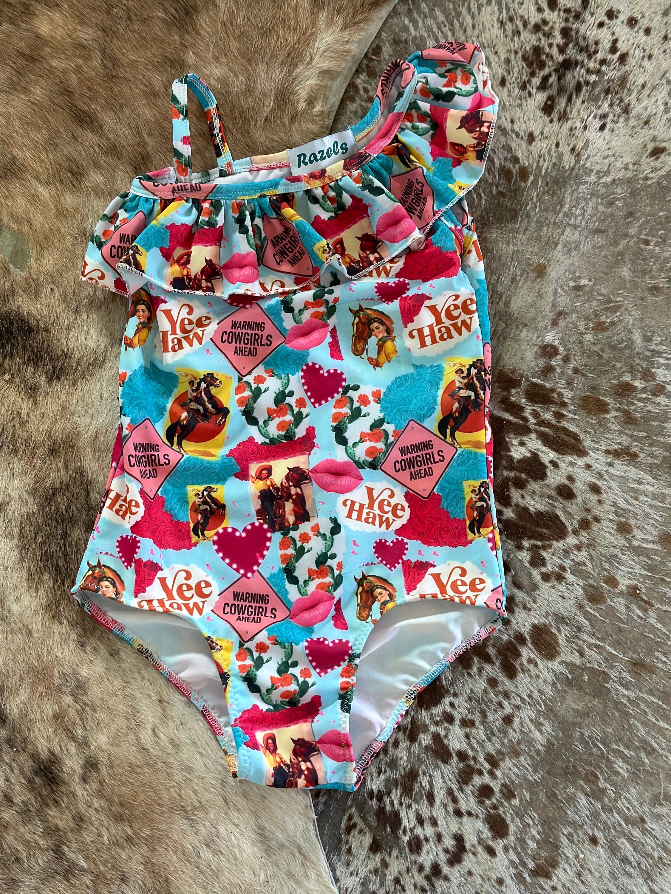 What a fun Cowgirl swimsuit!! 💗 Yeehaw!! Talk about Western Cutie! This fabulous 1-piece girls swimsuit features all the things we love about our Cowgirls - riding horses, hearts, cactus...a warning! So cute! I love this fabric so much it's also available in a girls blouse! 💞 • Available in sizes 0-3 months - 8/9!  • Double layered front More Razels! Check out all our Western swimsuits and sibling swimwear. Ships FREE with $35+ purchase.