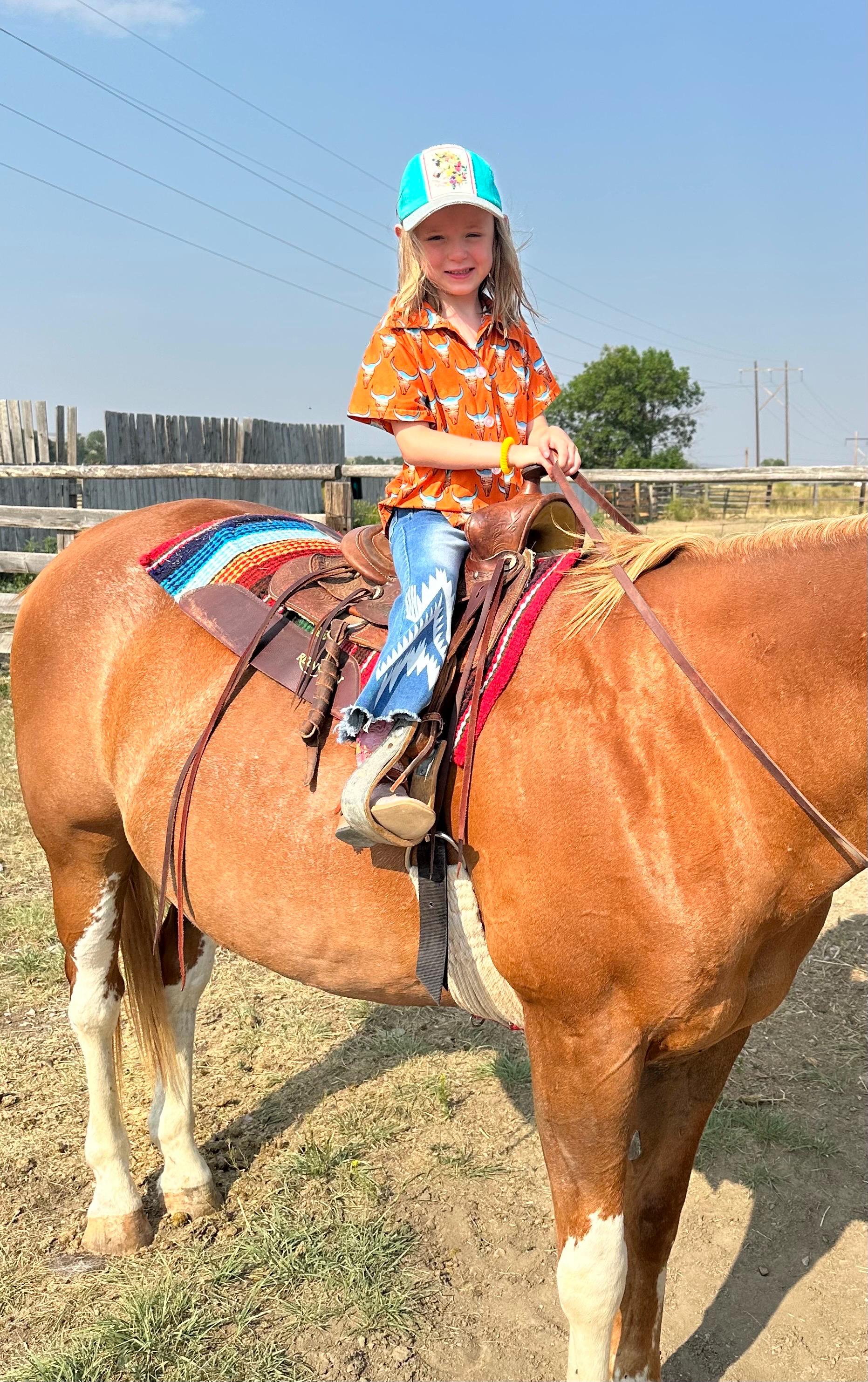 Check out this fun Kids Western button-up shirt featuring a unique desert highway scene inside steer heads. In a bold orange, this cowboy shirt perfectly blends cool and classic Western style—a shirt any cowkid would love! 🧡
