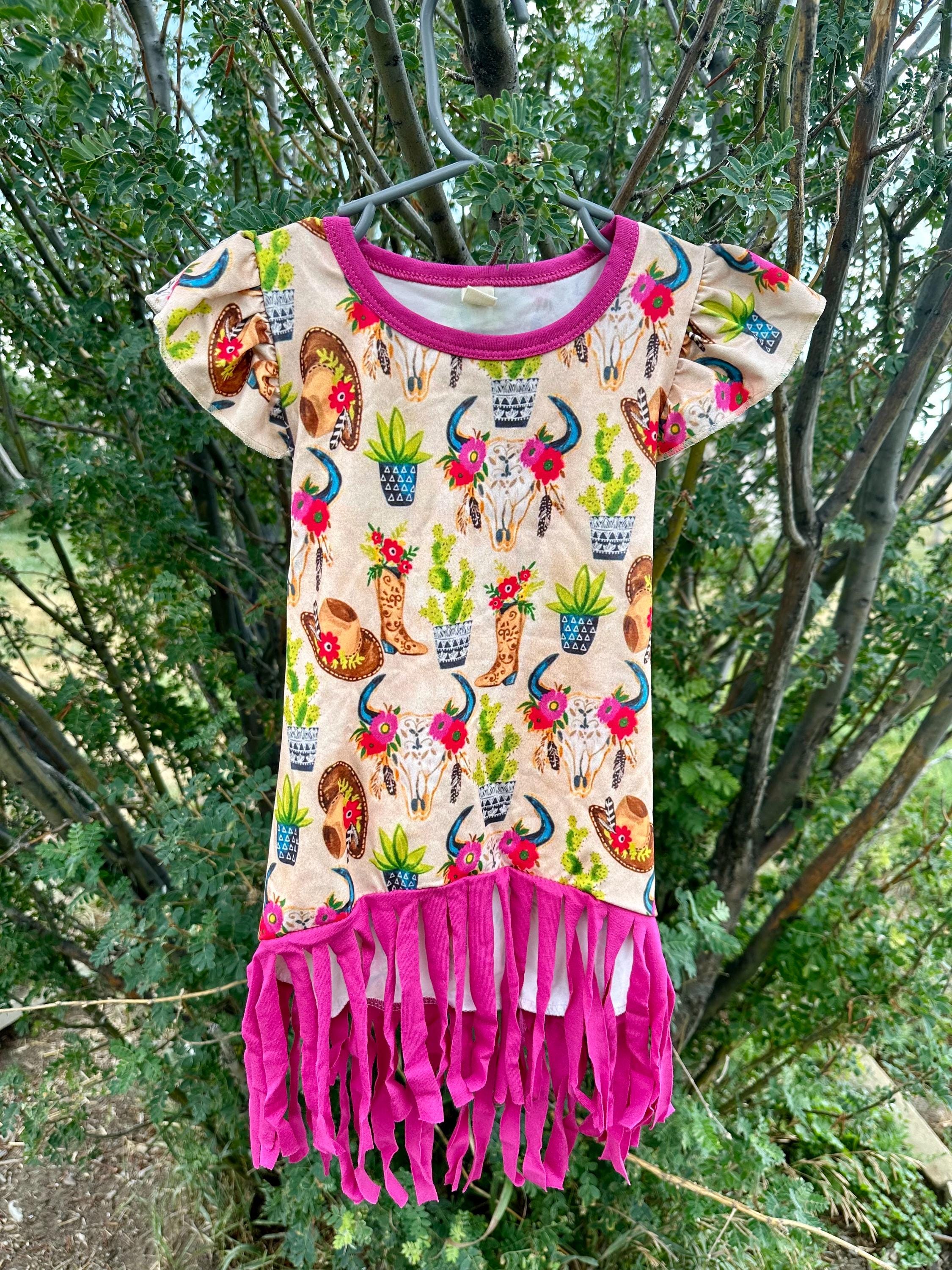 Cowgirl Fringe Dress โ The Perfect Western Tunic for Little Cowgirls features a vibrant western print, flutter sleeves, a charming tie-back, and thick pink fringe. Let your little cowgirl shine in this Cowgirl Fringe Tunic Dress!