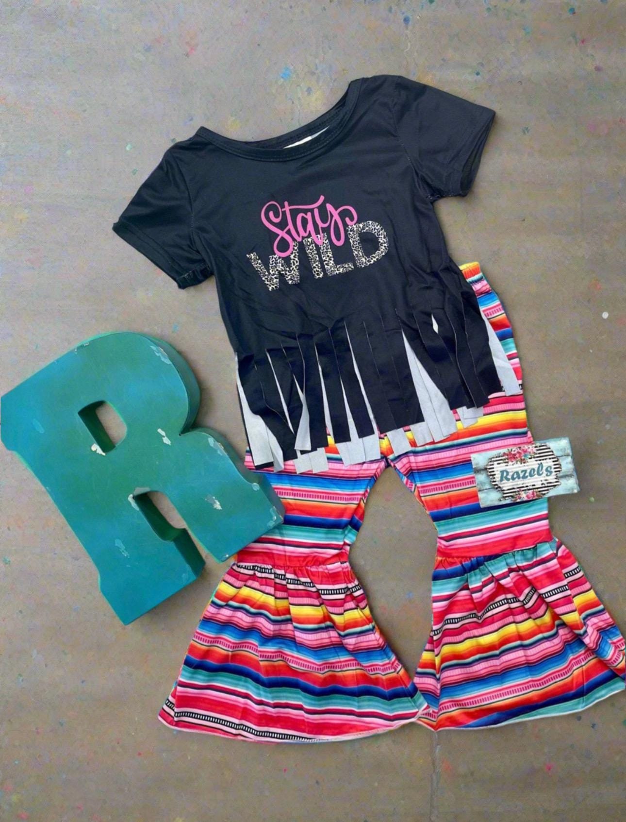 Stay Wild Girls Bell Bottom Set. Features a black Fringed Shirt with a bold "Stay Wild" design in pink and cheetah print, perfectly paired with vibrant serape-striped bell bottoms. Ships FREE with $35+ purchase.
