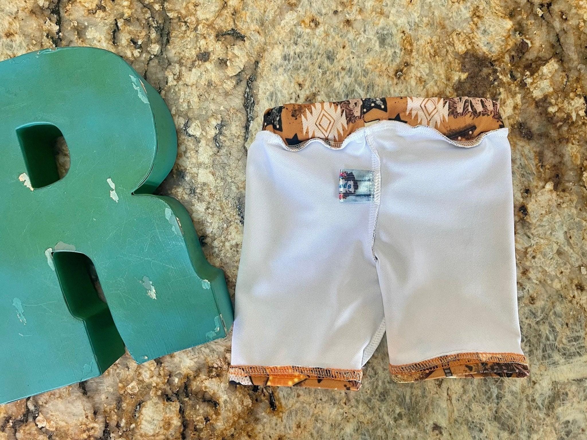High quality, matching WESTERN swimsuits for kids, featuring Mama Tried print with allover Mama Tried, Cacti, Arrows, Stars and Guitars in a country brown. Sibling Swimwear is available in boys swim trunks and girls ruffle bathing suit.