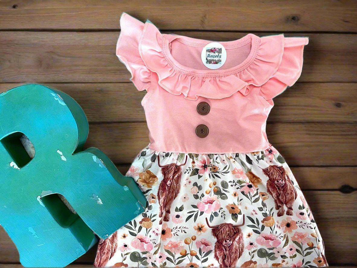 Girls Scottish highander cow dress features a sweet floral and highlander cow print skirt with a soft pink top with a ruffle collar, ruffle sleeves, and two button detail down the front. This fabric is also available in pjs and bell bottoms.