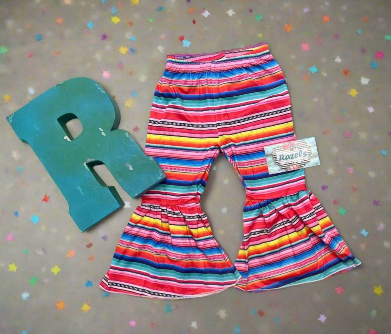 Stay Wild Girls Bell Bottom Set. Features a black Fringed Shirt with a bold "Stay Wild" design in pink and cheetah print, perfectly paired with vibrant serape-striped bell bottoms. Ships FREE with $35+ purchase.