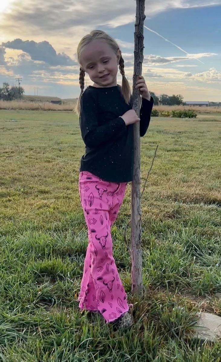 Jernie modeling girls hot pink western jeans. Jeans feature black steerheads, arrows, and cacti in an awesome western motif. Jeans have an adjustable waistband, pockets, and a frayed bell bottom hem.
