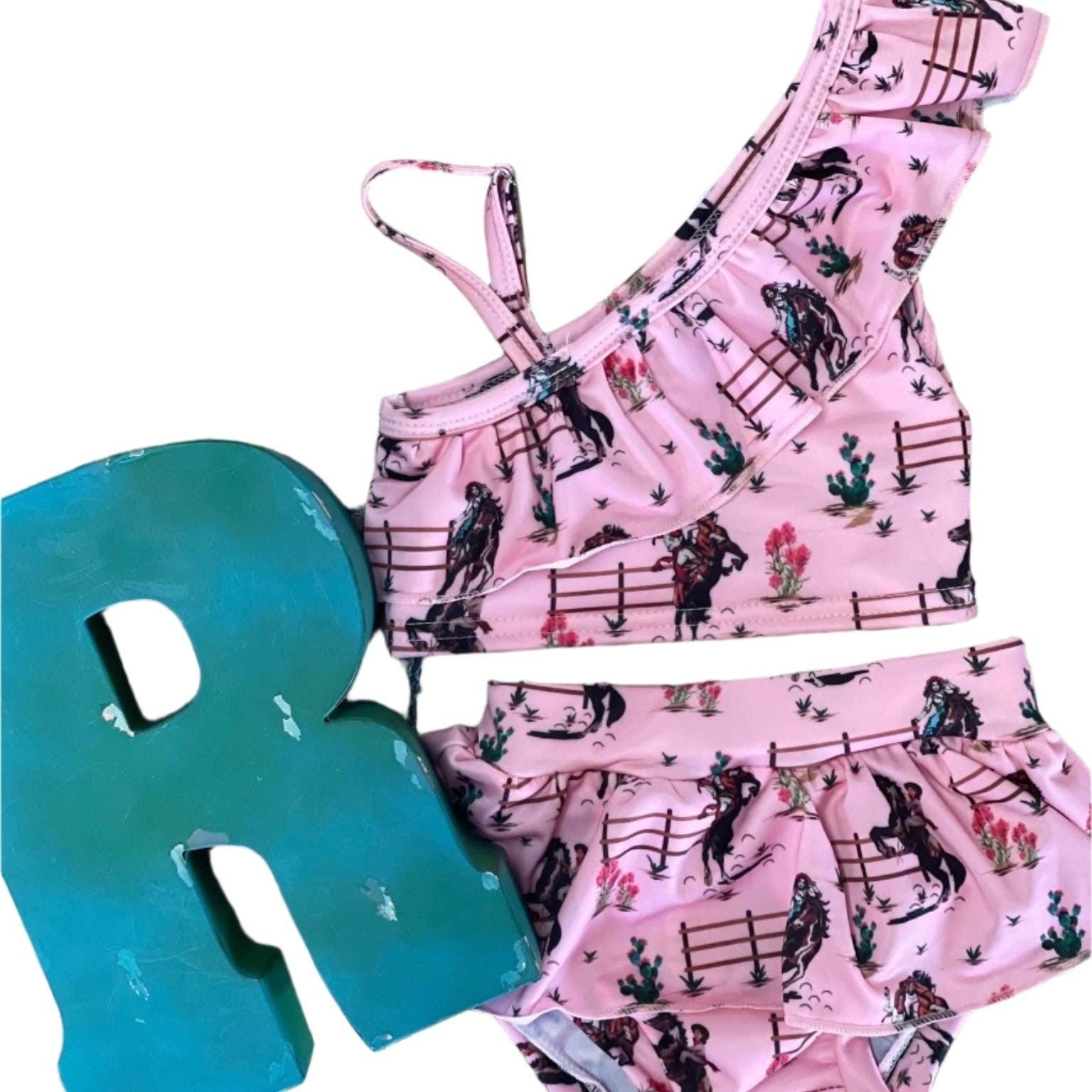 Saddle up for summer with this Pink Cowgirl Swimsuit! This Western Ruffled Swimsuit features vintage cowgirls, adorable ruffles, and a bold Wild West vibe, perfect for little adventurers. Designed for comfort and durability, it includes adjustable straps, a fully lined front, and high-quality swimsuit material. Available in sizes 0-3 months to 6/7, this Cowgirl Bathing Suit is ideal for babies and toddlers. FREE U.S. shipping on $35+ orders. Shop Razels for the best Western Bikini today!