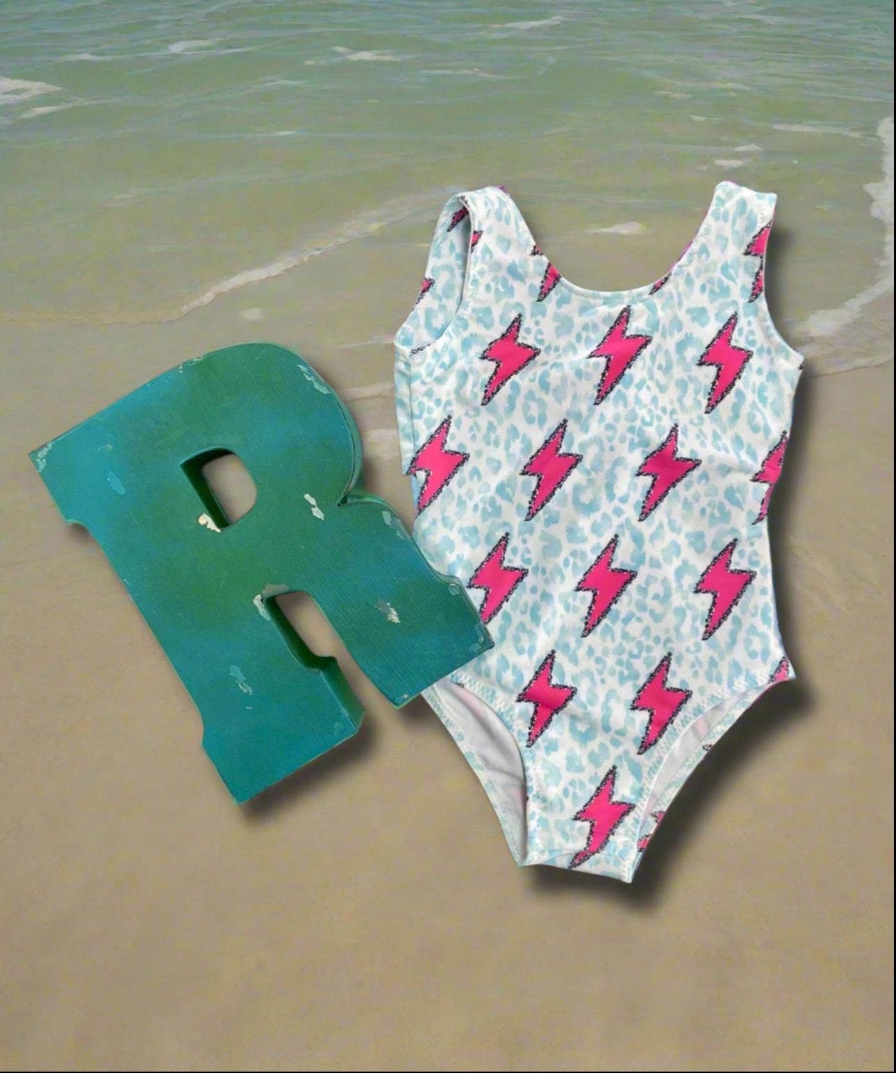 Pink Lightning Bolt One- piece Swimsuit is a Turquoise Cheetah Print One-Piece swimsuit featuring a striking pink lightning bolts and turquoise cheetah print design with a tie-back detail. Available in sizes 0/3 months to 8/9 years. Ships FREE $35+