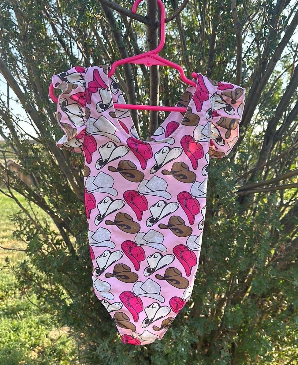 Cowgirl Swimsuit | Pink Cowgirl Hat Swimsuit | Western Swimsuits Girls, Sweetheart of the Rodeo
The cutest Cowgirl Swimsuit is here! Featuring hot pink, silver, and brown cowgirl hats on a bubblegum pink background, this one-piece swimsuit is a must-have for little rodeo queens. The flutter neckline adds the perfect touch of sweetness, making it as adorable as it is stylish!
Ships FREE FROM MONTANA with any $35+ purchase!