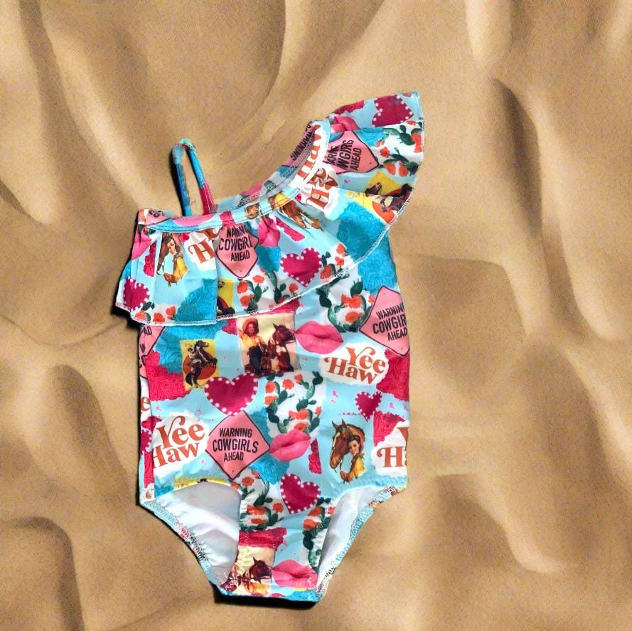 Yeehaw, Cowgirl Cutie! 🤠💗 This fun and fabulous Western Ruffled Swimsuit is perfect for little cowgirls who love adventure! Featuring a darling print of cowgirls riding horses, hearts, and cacti, this one-piece swimsuit is as cute as it gets. ✨ Why You’ll Love It: ✔️ Available in sizes 0-3 months to 8/9 – perfect for babies, toddlers, and big sisters! ✔️ Double-layered front for comfort and durability. ✔️ High-quality swimsuit material that’s made to last. 📦 FREE U.S. shipping on orders $35+