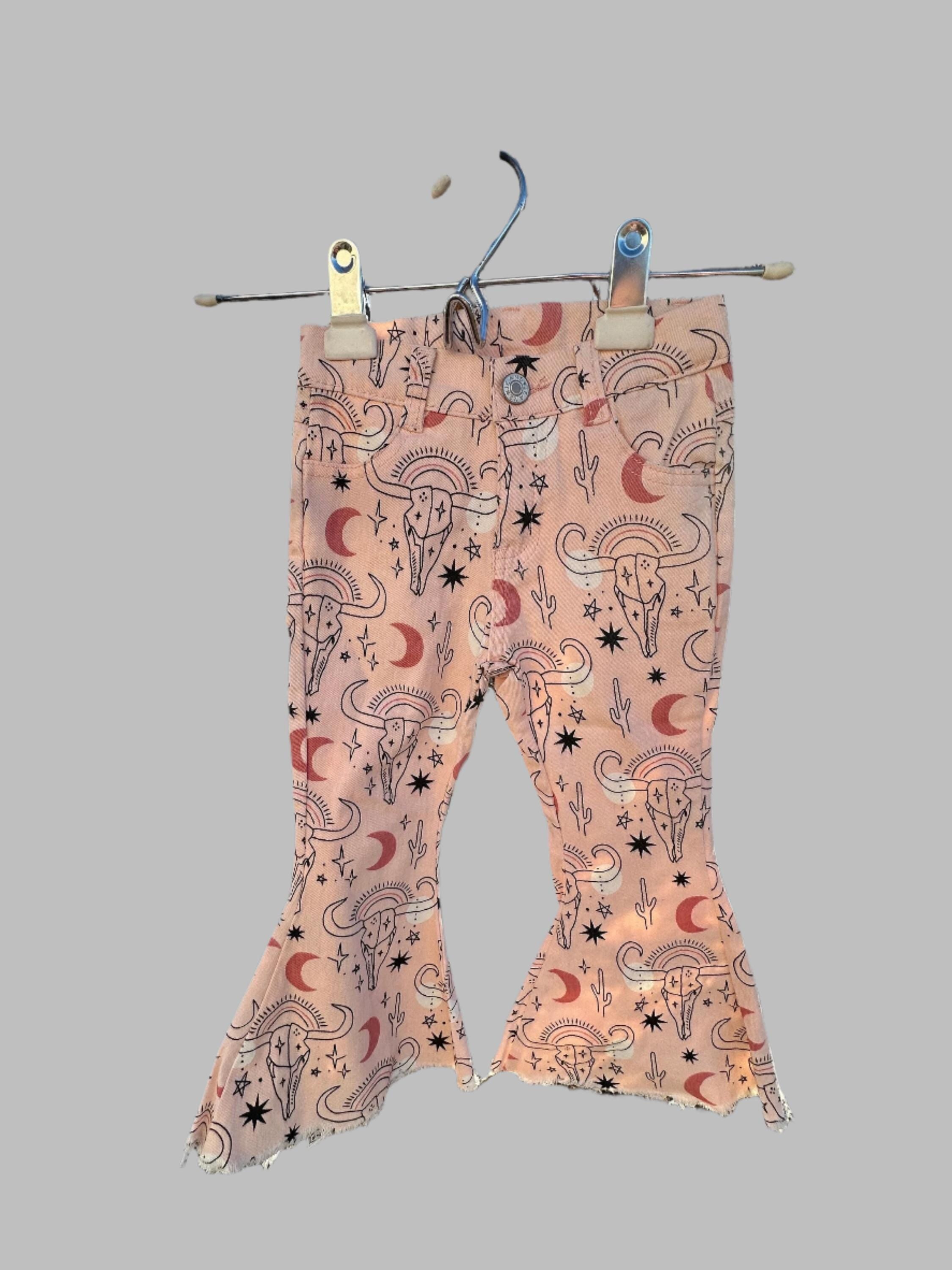 Cowgirl Pink Bell Bottoms – Western Cow Skull Jeans (ONLY 2T, 3T, 4T LEFT!) New cowgirl jeans just dropped—and aren’t they fabulous?! 💓 With cow skulls, moons, cactus, stars... oh my! These pink bell bottoms are full of western sass and sweet desert vibes. ✓ Functional front and back pockets ✓ Adjustable waistband for a perfect fit ✓ Stretchy cotton/spandex blend for all-day comfort ✓ Button and zipper closure ✓ Frayed hems for that trendy flair
