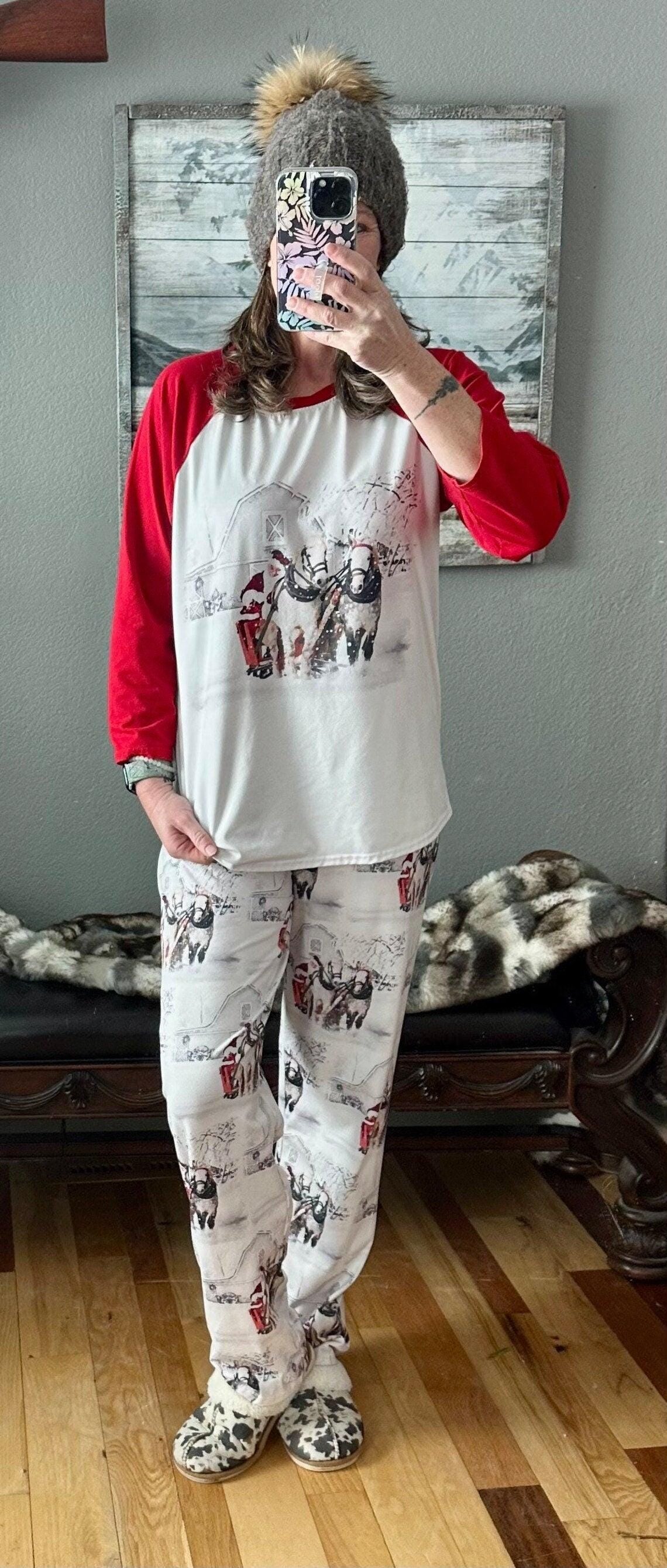 Family White Christmas Pajamas feature Santa Claus at the reins of a horse-drawn sleigh, pulling away from a vintage barn on a snowy winter day. The top has coordinating red raglan sleeves, and the bottoms feature a festive Santa print all over