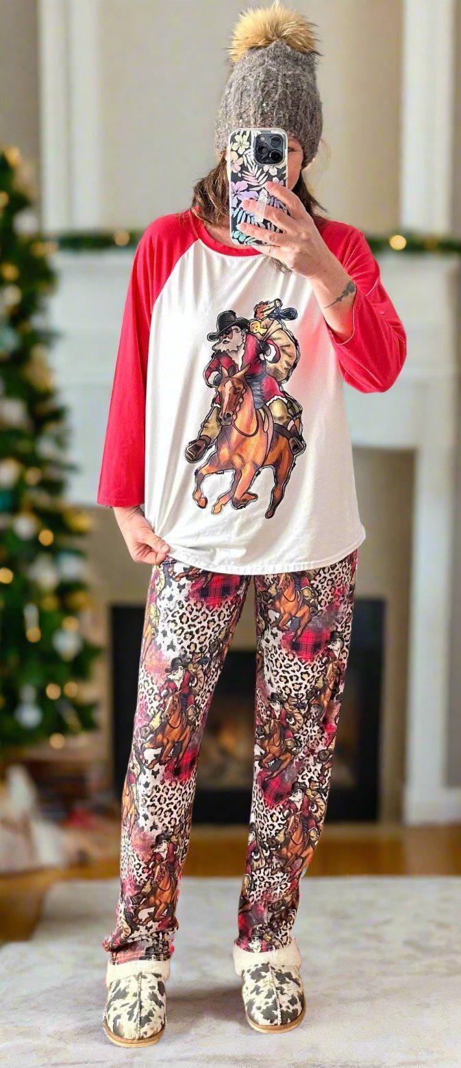 family cowboy Santa Christmas pajamas feature a raglan-style top with Santa riding his best horse, carrying a sack of packages. The top has red sleeves and neckline. The bottoms have an all-over cheetah print, buffalo plaid and Santa on his horse